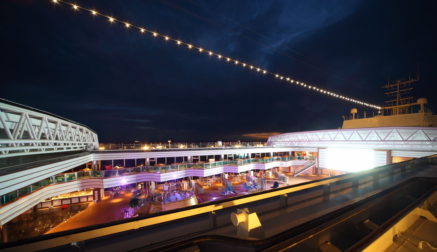 People enjoy night party on the deck of illuminated cruise ship