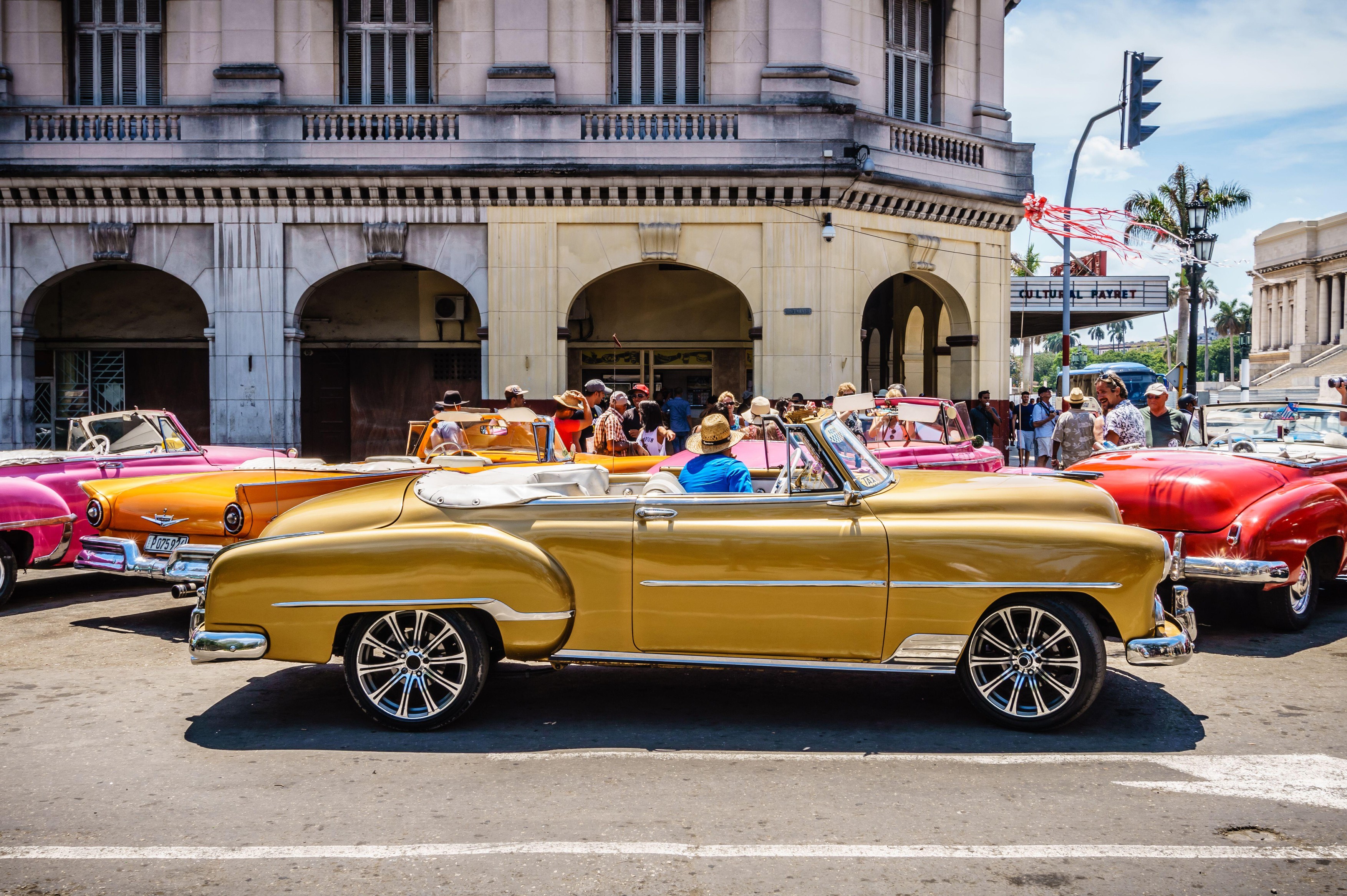 A row of vintage cars are parked on a street. The cars are of different colors and styles, and a man is sitting in the middle of the row. Concept of n