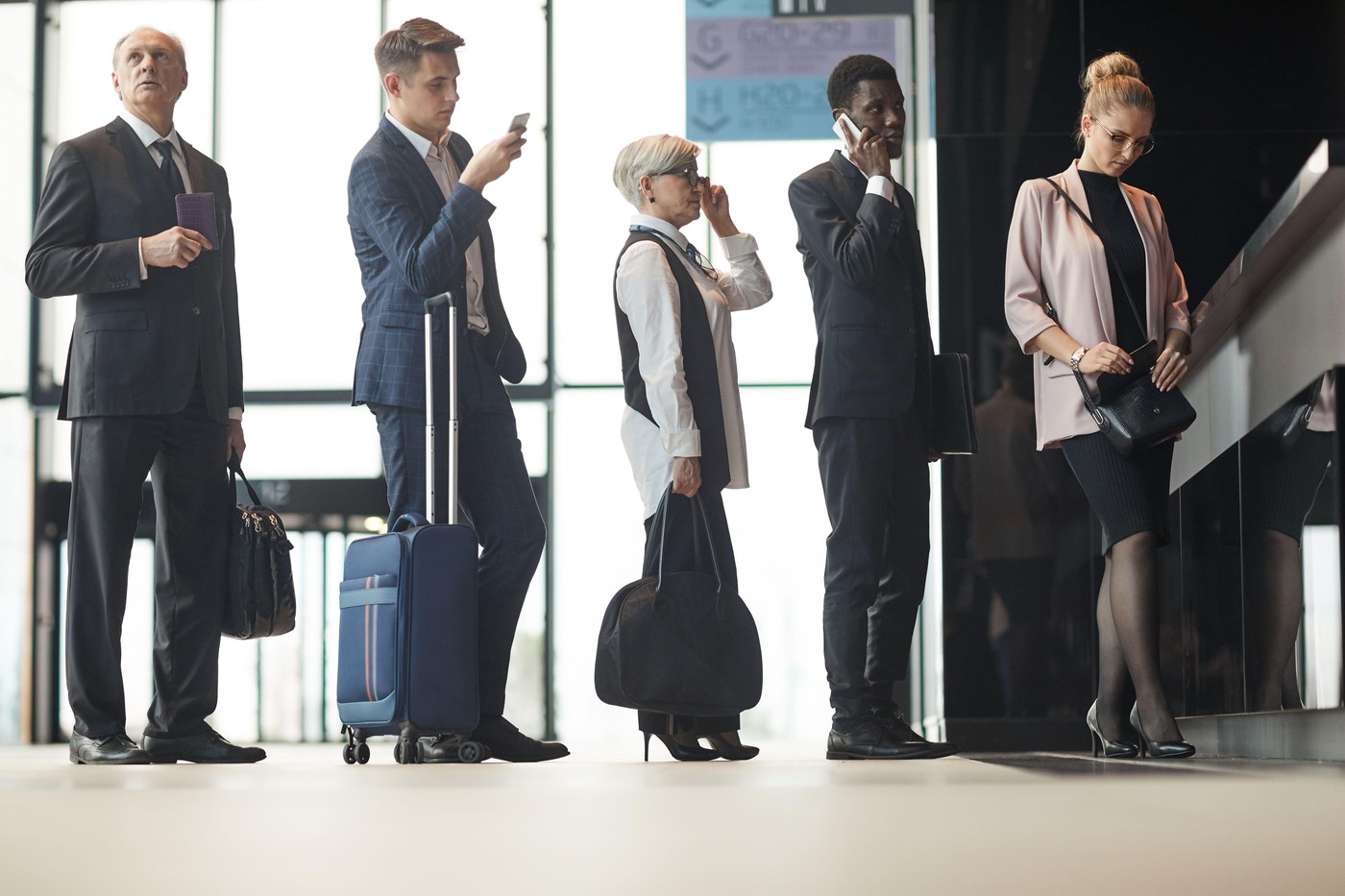 Group of business people with luggages standing in a queue and registering on the reception at the airport