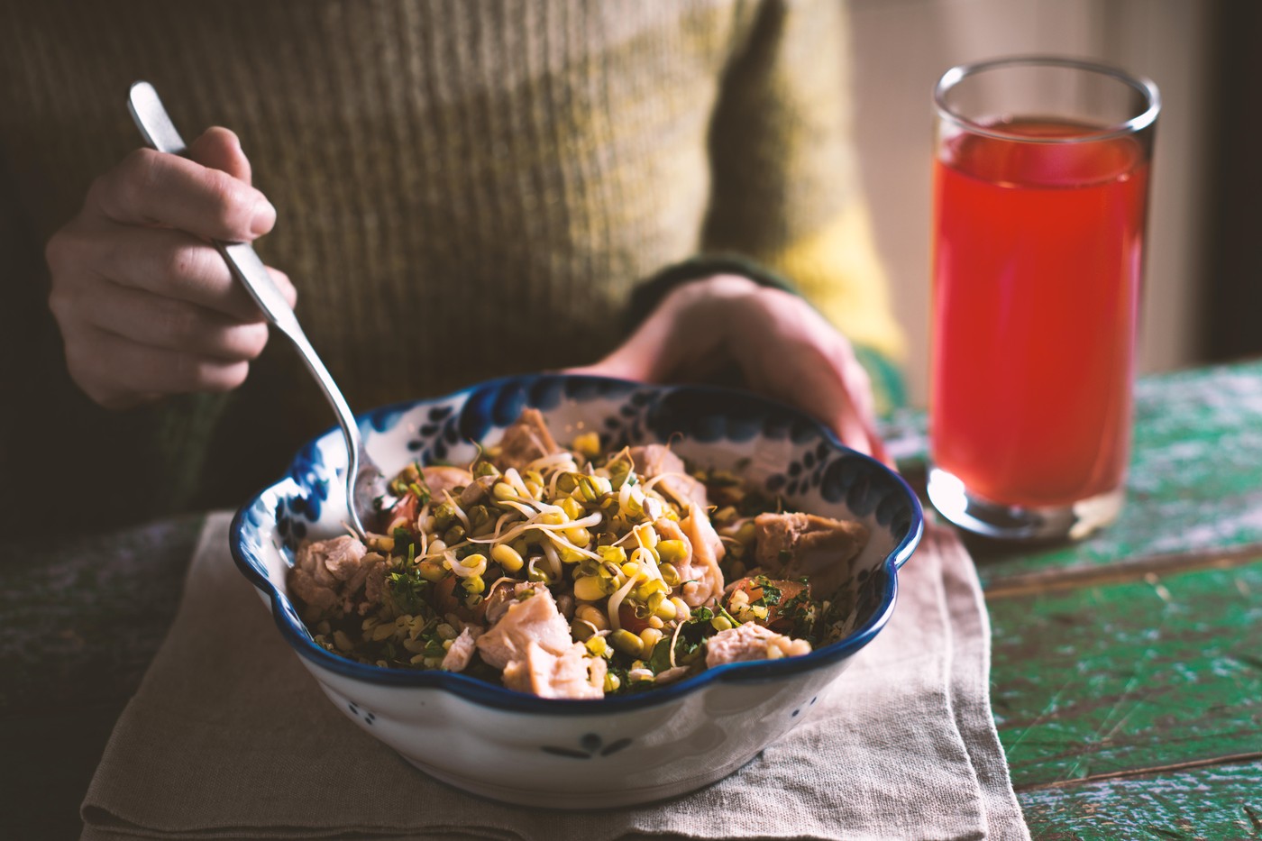Woman in a green sweater eating a salad with chicken and beans horizontal
