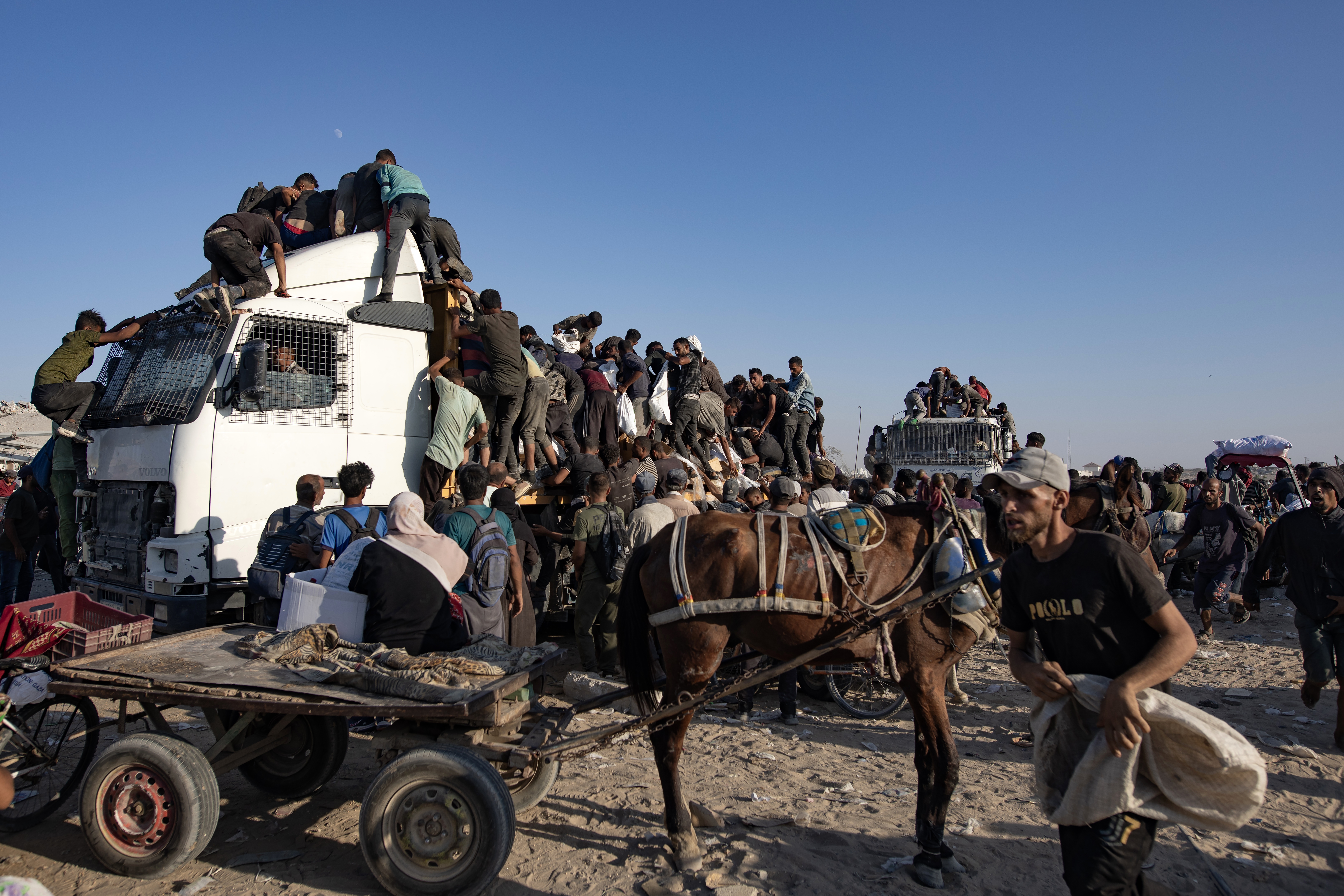 epa12283320 Internally displaced Palestinians climb aid trucks to get food near a food distribution point in the Morag corridor, south of Khan Younis, in the southern Gaza Strip, 04 August 2025.  EPA/HAITHAM IMAD