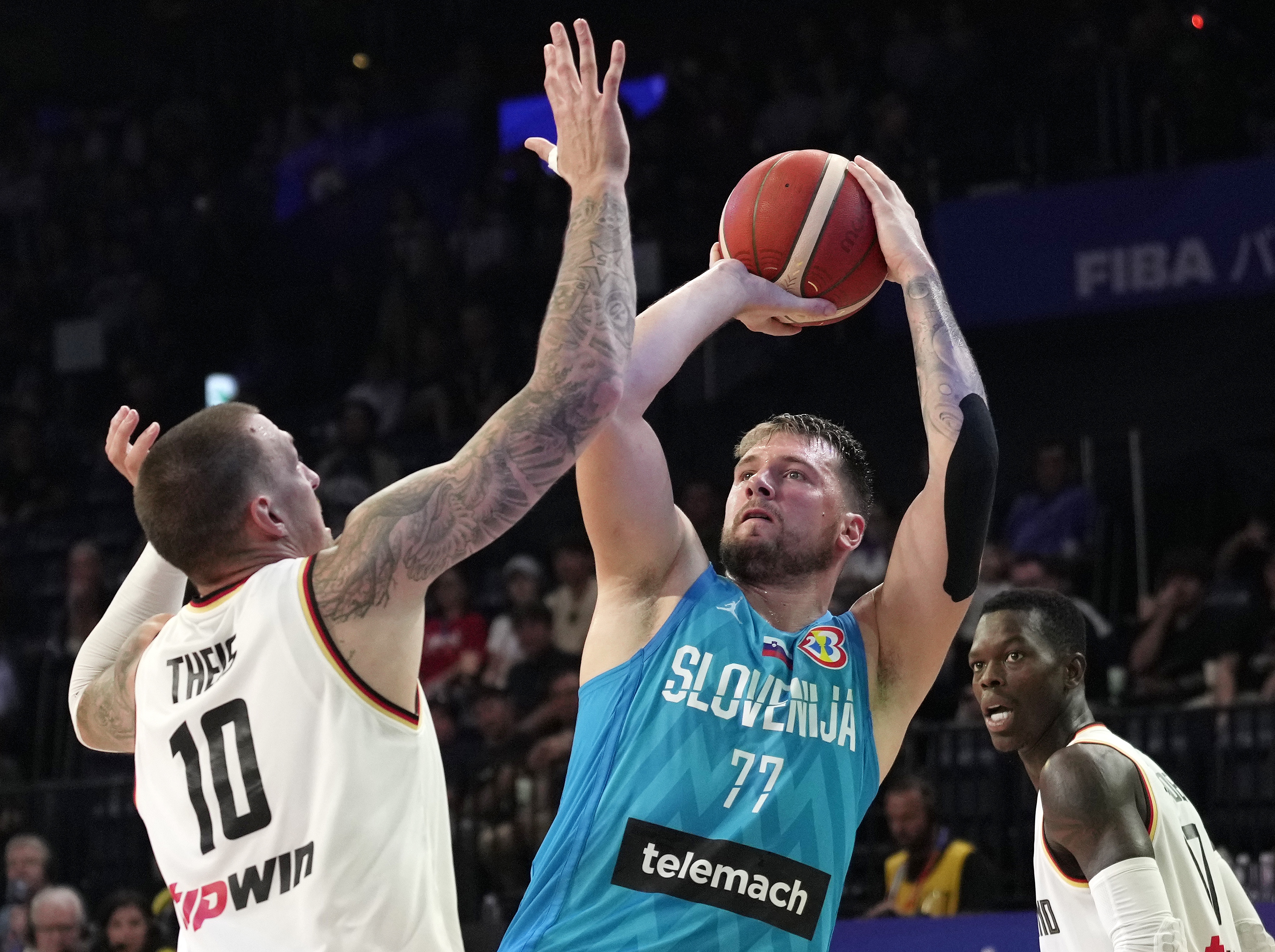 epa10837491 Daniel Theis (L) of Germany tries to block a shot by Luka Doncic (C) of Slovenia during the FIBA Basketball World Cup 2023 second round match between Germany and Slovenia in Okinawa, Japan, 03 September 2023.  EPA/KIMIMASA MAYAMA