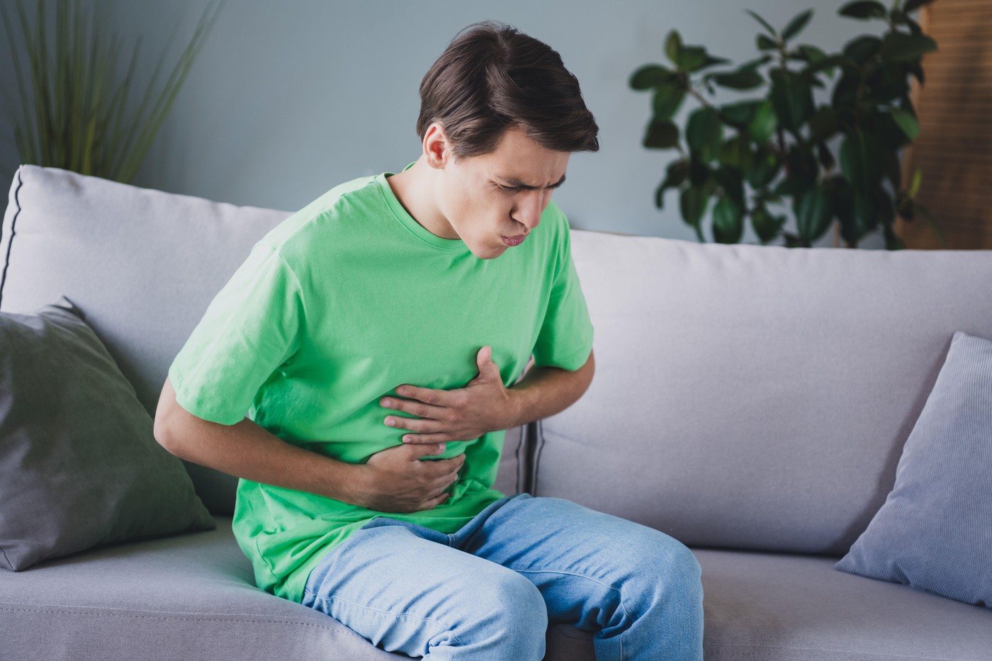 Young Man Experiencing Discomfort Sitting Indoors on a Sofa in a Relaxed Home Setting