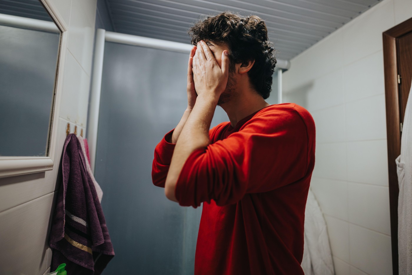 Man in bathroom preparing for day wearing red sweater
