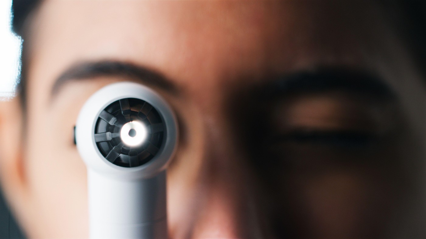 Close Up Portrait Of Female Ophthalmologist In Hospital Looking Through Ophthalmoscope