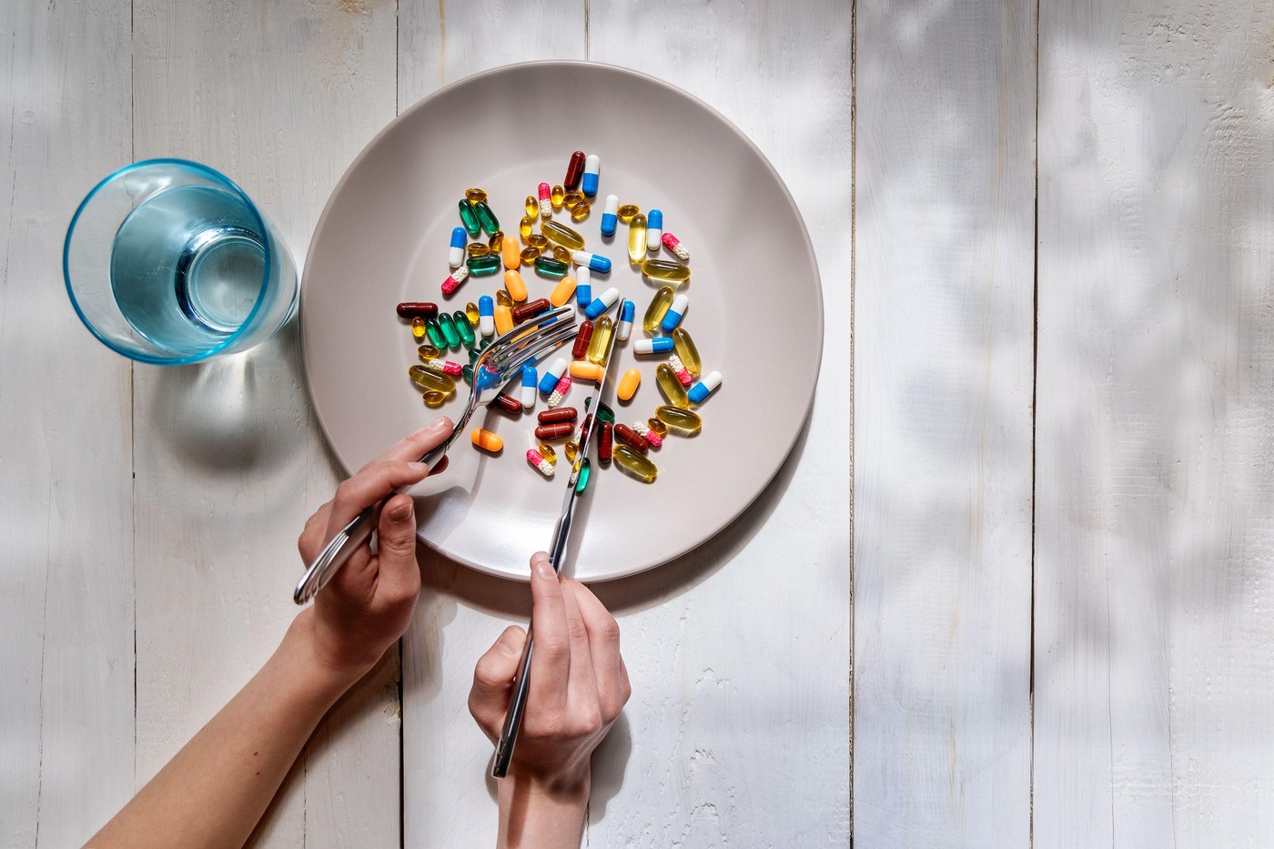 Hands eating pills with fork and knife. A person uses fork and knife to eat colorful pills from a plate, symbolizing modern reliance on supplements