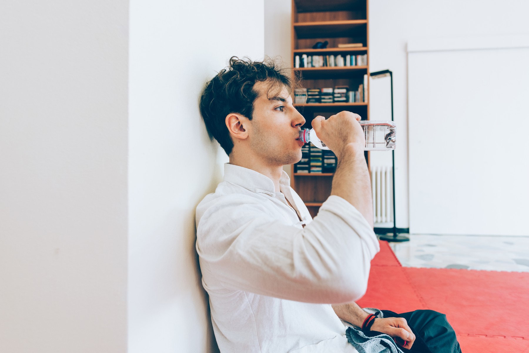 Man sitting leaning against column drinking water from bottle