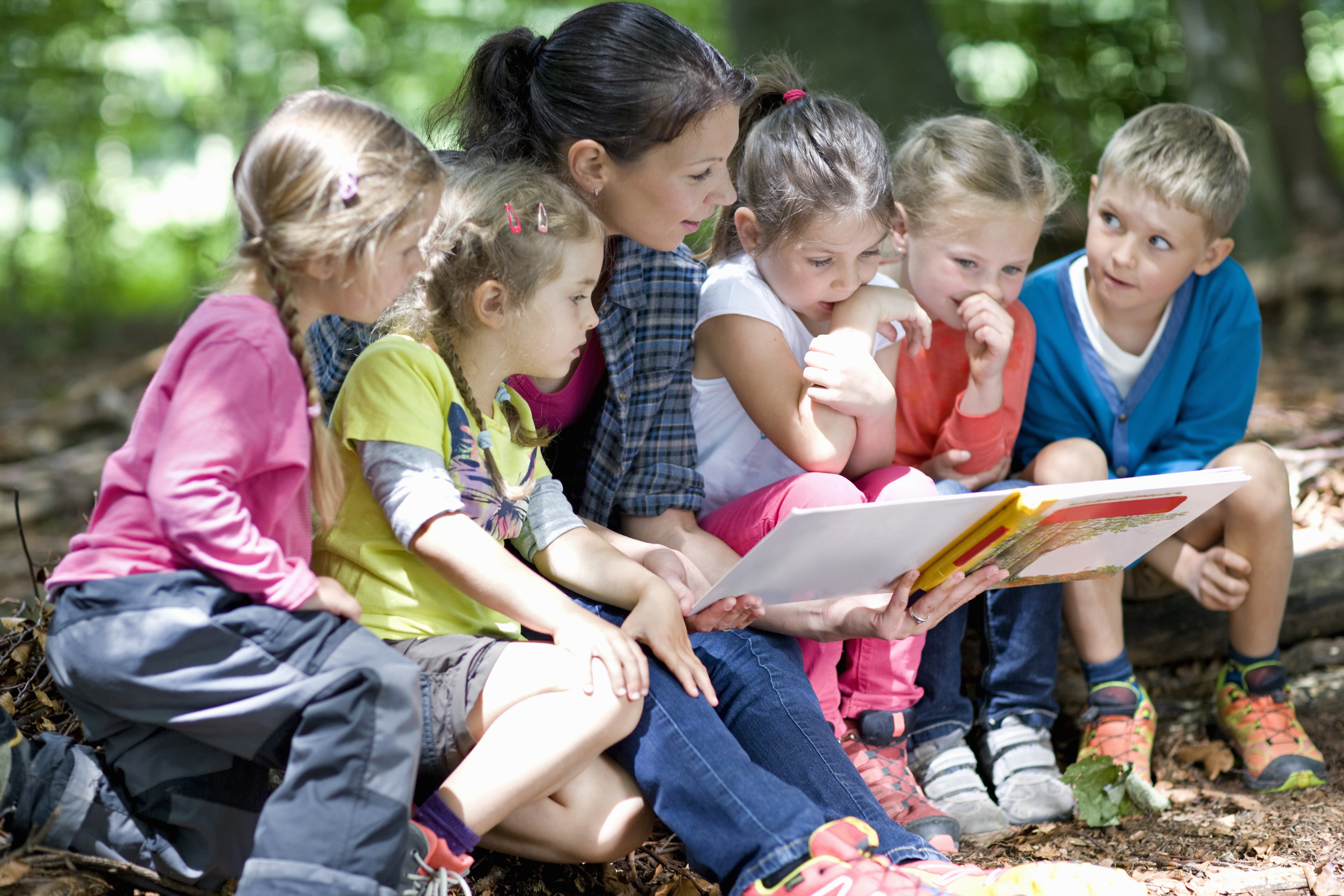 Kindergarten,Teacher,Reading,With,Kids,In,A,Wood,Kindergarten