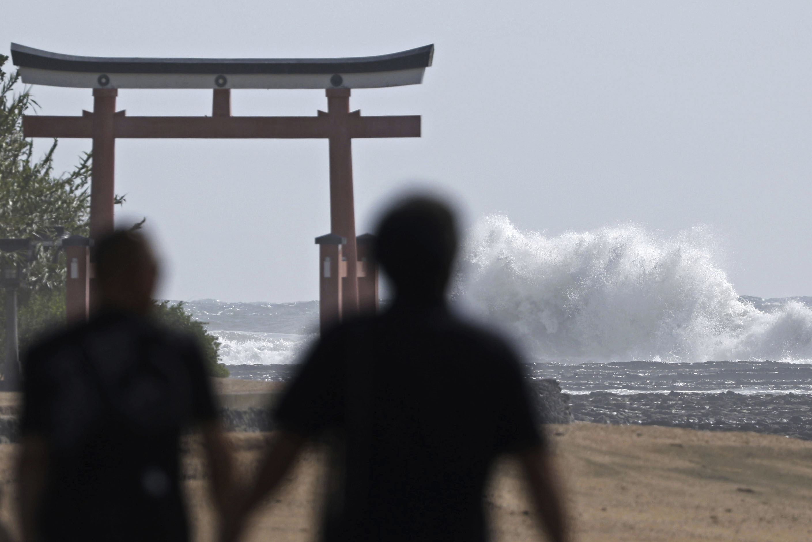 People walk near a "torii" gate of a shrine while waves hit a coastal area in Miyazaki, western Japan, Tuesday, Aug. 27, 2024, as a typhoon is approaching. (Hidetaka Komukai/Kyodo News via AP)