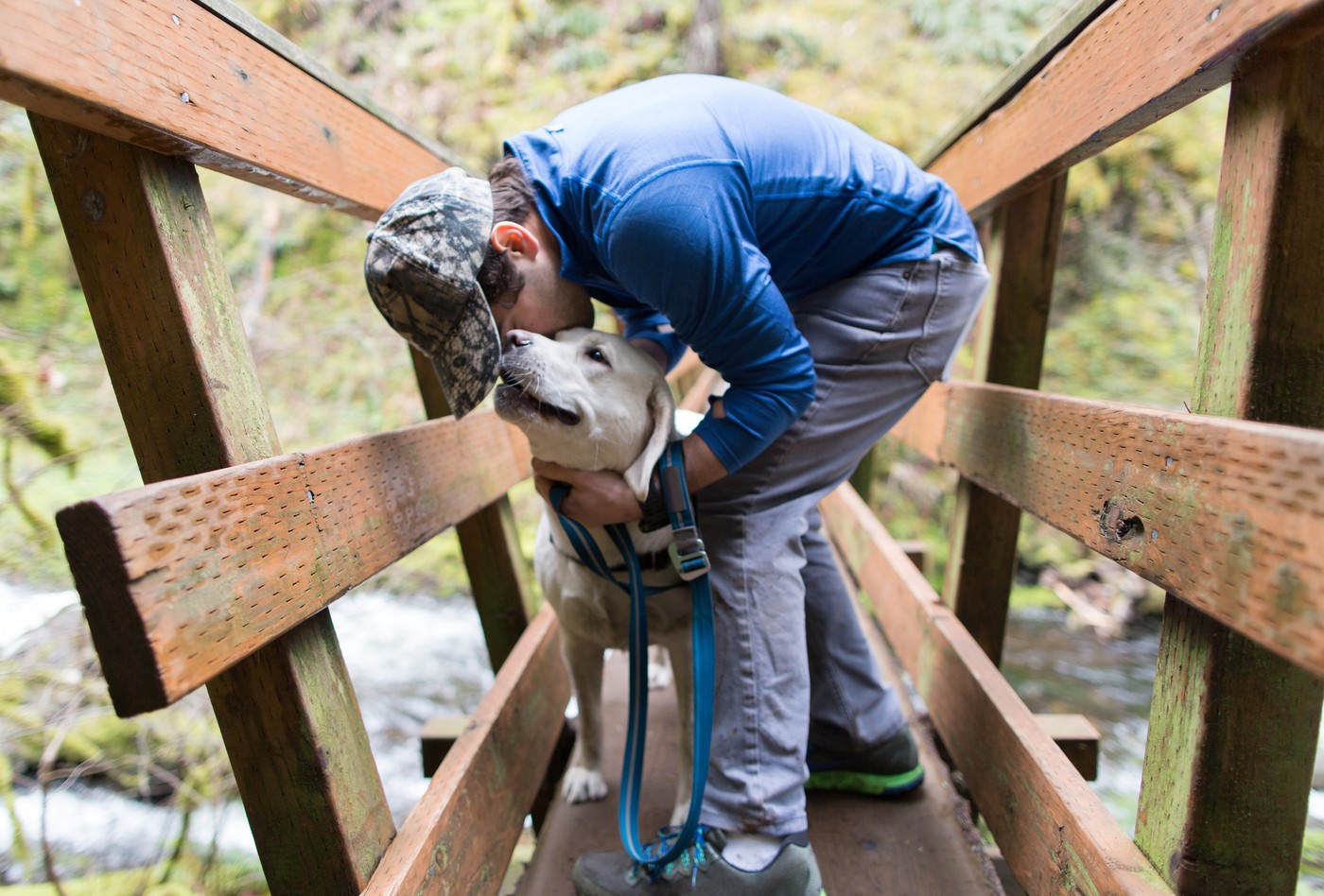 Man on wooden footbridge kissing dog