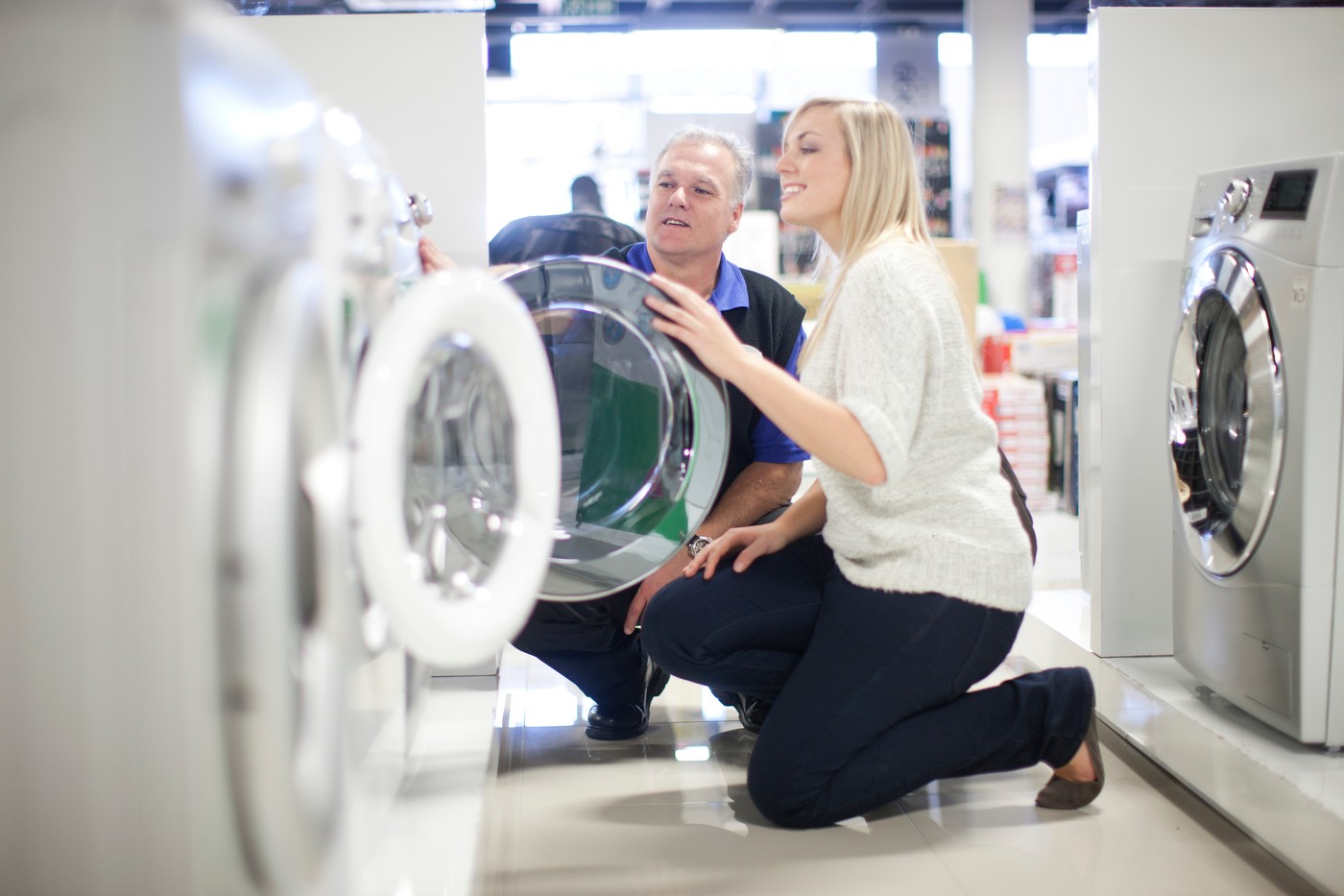 Young woman and salesman looking at washing machines in showroom