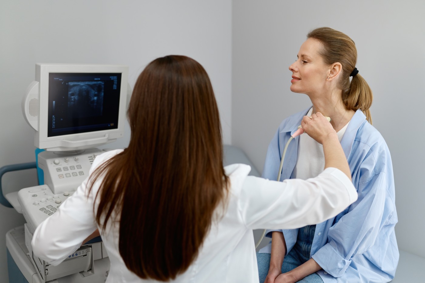 Woman doctor conducting ultrasound of thyroid gland and lymph nodes