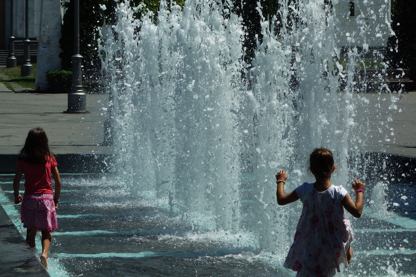 Two girls dancing and playing in fountain in summer day