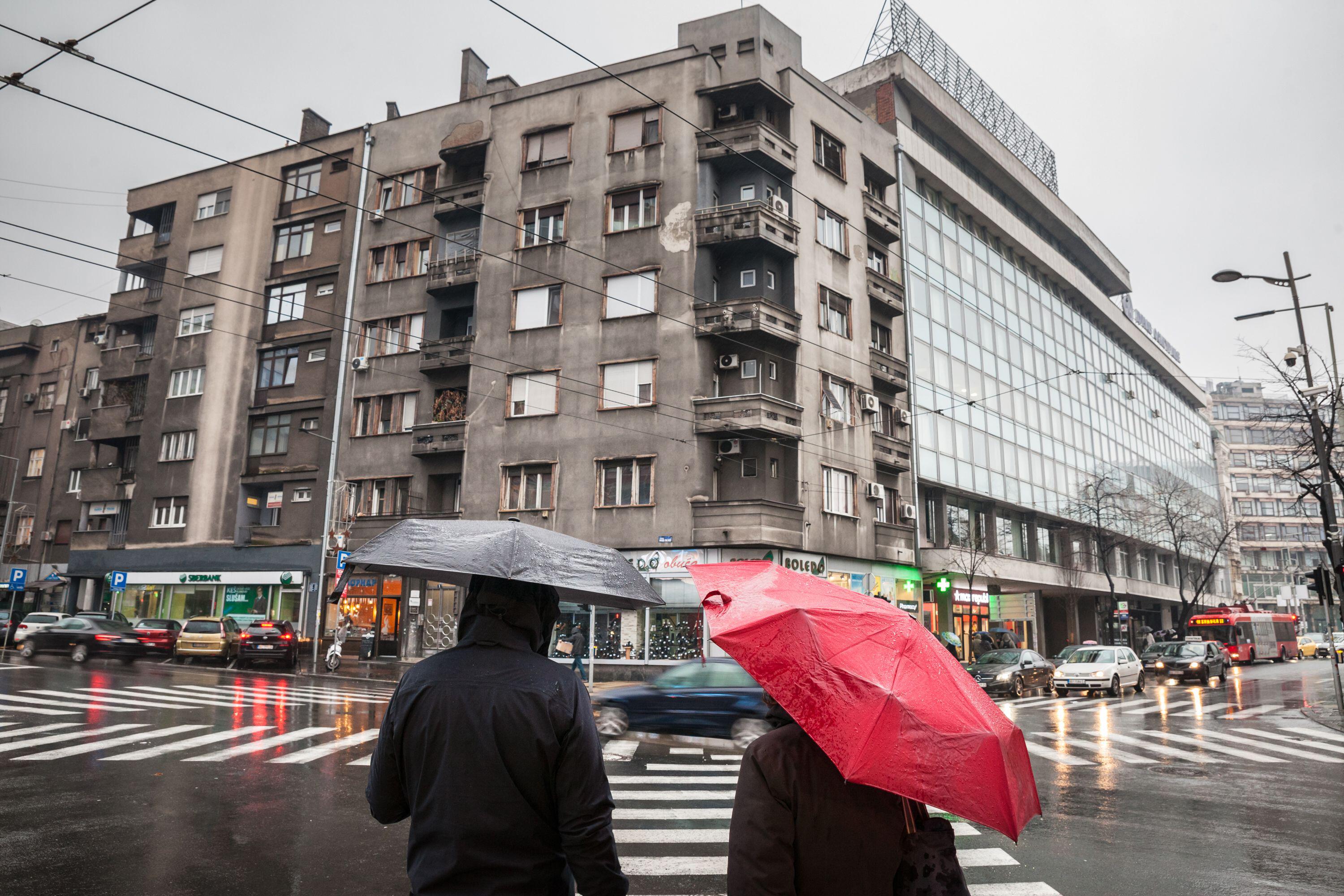 Picture of people with an umbrella waiting for green light to cross a crossroad in the city center of Belgrade, during heavy rains, in autumn.
