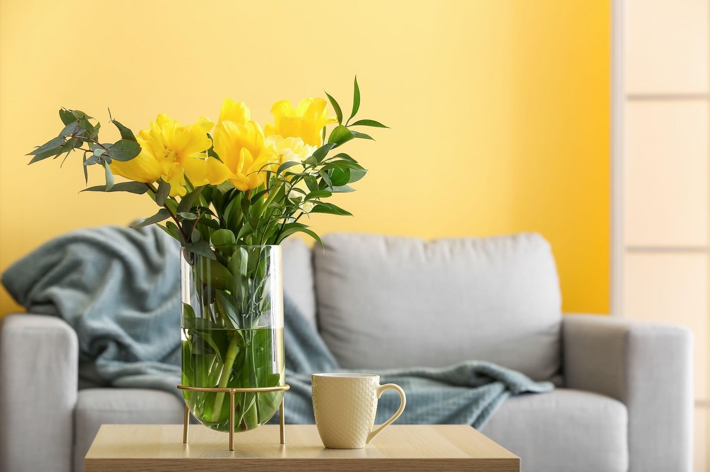 Vase with yellow flowers and cup on table in living room