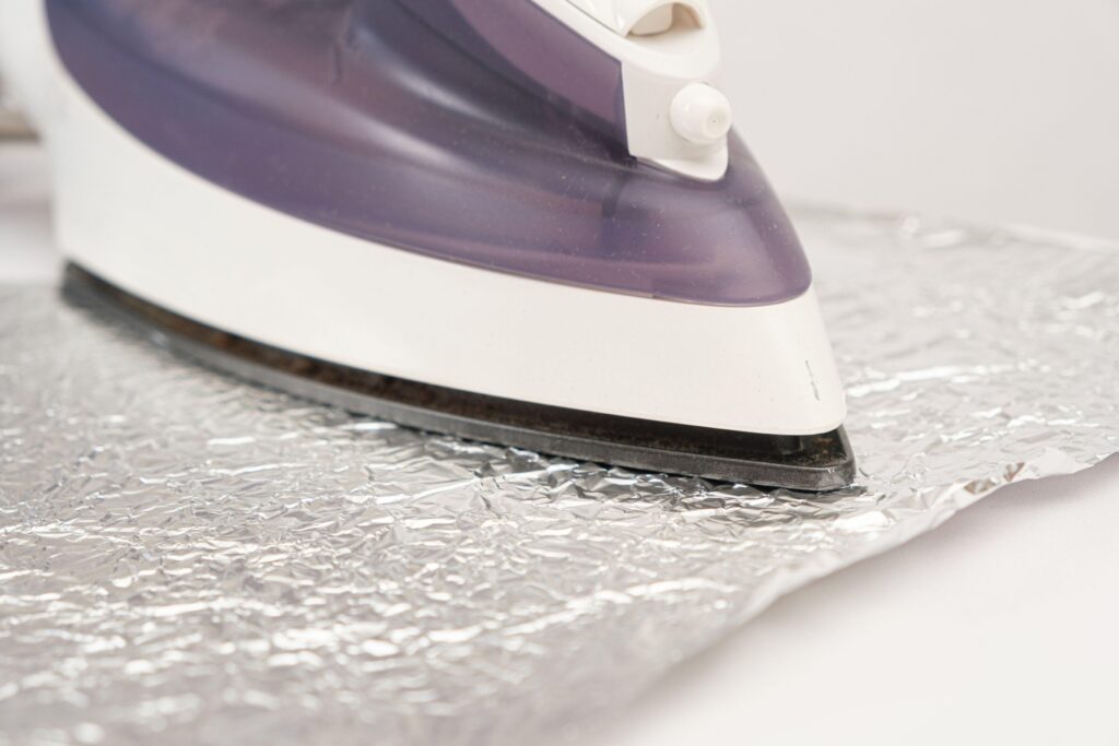 The iron irons the foil on a white background. Cleaning the sole of the iron from carbon deposits by folk methods,Image: 674085037, License: Royalty-free, Restrictions: , Model Release: no, Credit line: / Alamy / Alamy / Profimedia