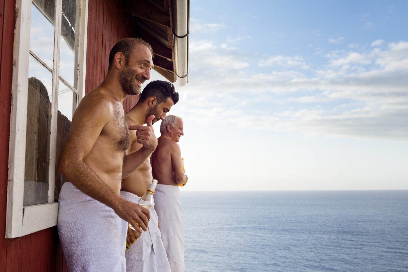 Three male friends standing outside sauna enjoying beer