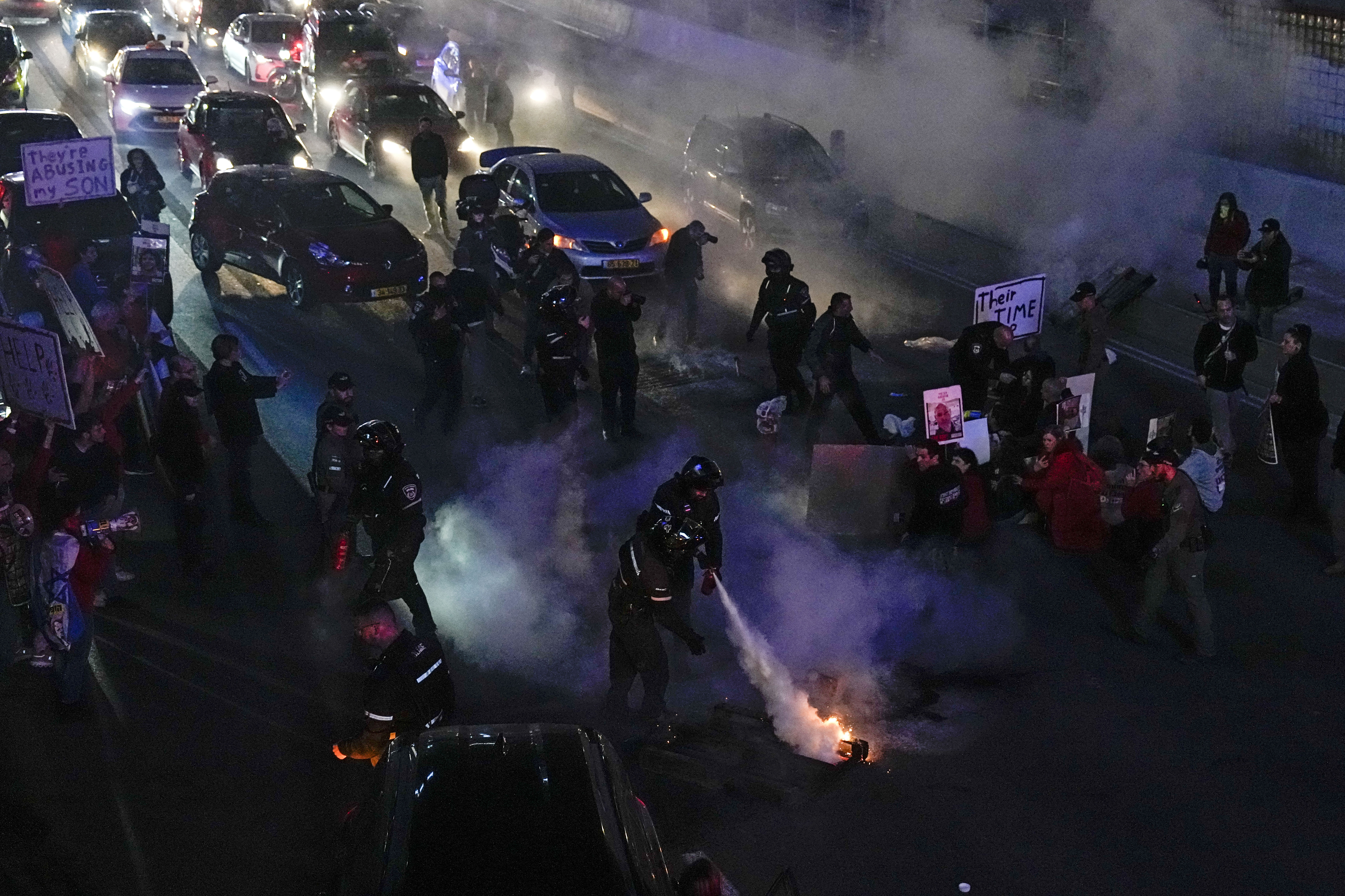 Police officers extinguish the fire set on a barricade during a protest to demand the release of the hostages taken by Hamas militants into the Gaza Strip during the Oct. 7th attack, in Tel Aviv, Israel, Saturday, Feb. 10, 2024. (AP Photo/Ariel Schalit)