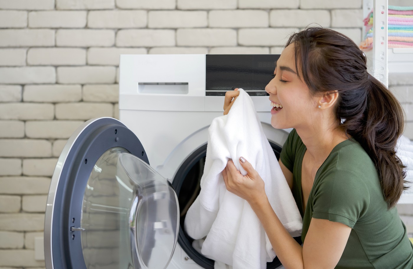 Asian housewife inhaled the smell of white cloth that was just washed from the washing machine. Working atmosphere in the laundry room.
