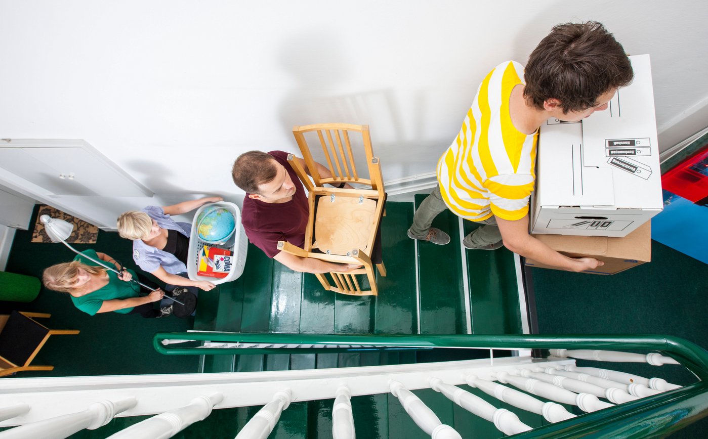 Young people moving in to a new apartment. Friends help carrying moving boxes, furniture and things upstairs to the new flat.