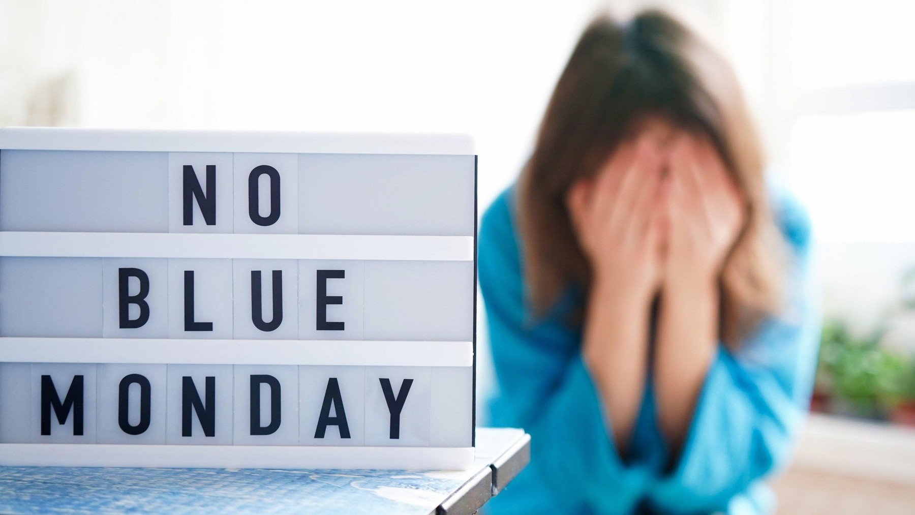 White board with text no blue monday on the table, in the background a woman in blue clothes depressed near the window,defocused.Blue monday day banne
