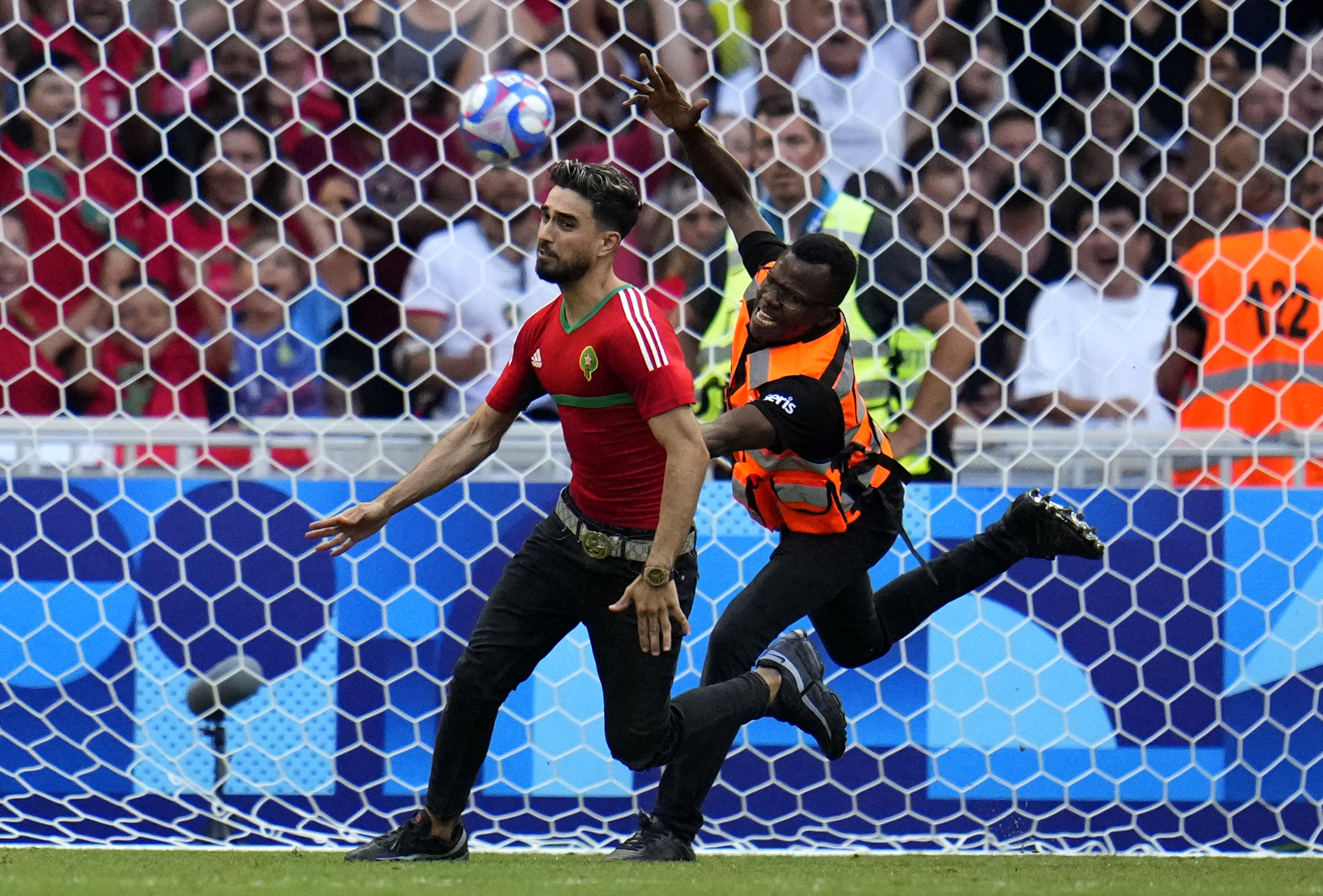 A spontaneous man is chased by security personnel during a men's semifinal soccer match between Morocco and Spain at the 2024 Summer Olympics, Monday, Aug. 5, 2024, at Marseille Stadium in Marseille, France. (AP Photo/Julio Cortez)