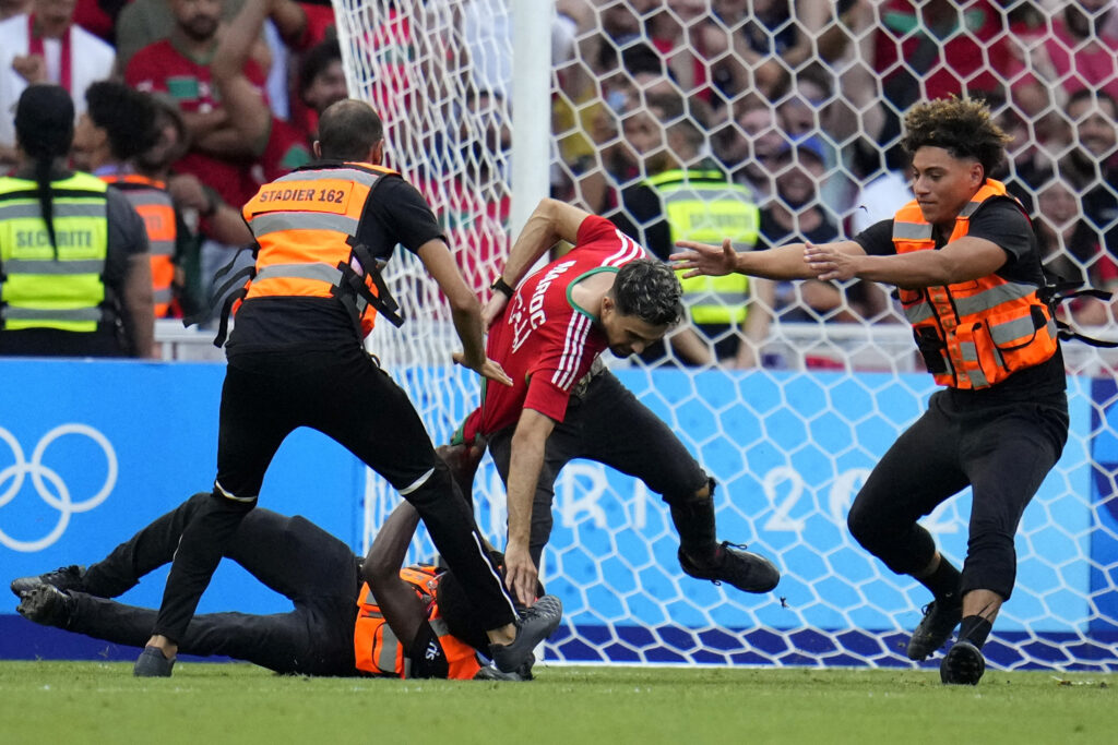 A spontaneous man is chased by security personnel during a men's semifinal soccer match between Morocco and Spain at the 2024 Summer Olympics, Monday, Aug. 5, 2024, at Marseille Stadium in Marseille, France. (AP Photo/Julio Cortez)
