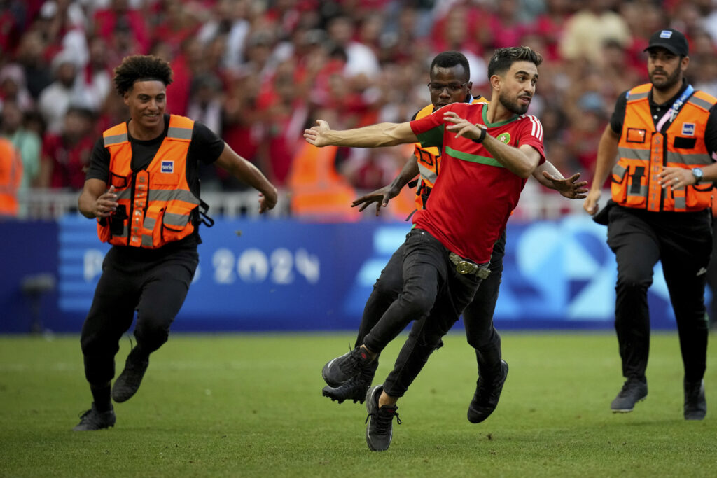 A spontaneous man is chased by security personnel during a men's semifinal soccer match between Morocco and Spain at the 2024 Summer Olympics, Monday, Aug. 5, 2024, at Marseille Stadium in Marseille, France. (AP Photo/Daniel Cole)