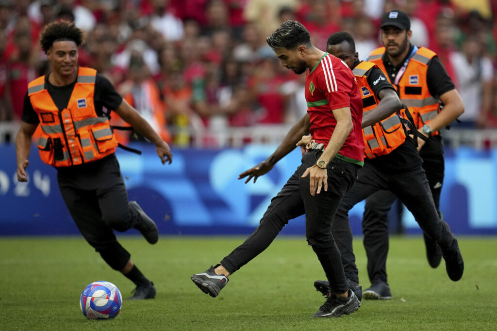 A spontaneous man is chased by security personnel during a men's semifinal soccer match between Morocco and Spain at the 2024 Summer Olympics, Monday, Aug. 5, 2024, at Marseille Stadium in Marseille, France. (AP Photo/Daniel Cole)