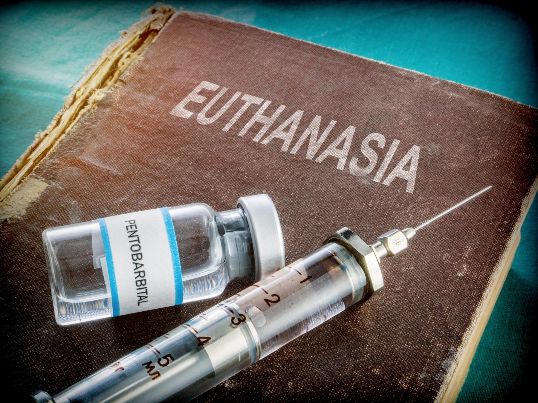 Eutanazija Vial and vintage syringe with medicine on an old book of euthanasia, conceptual image