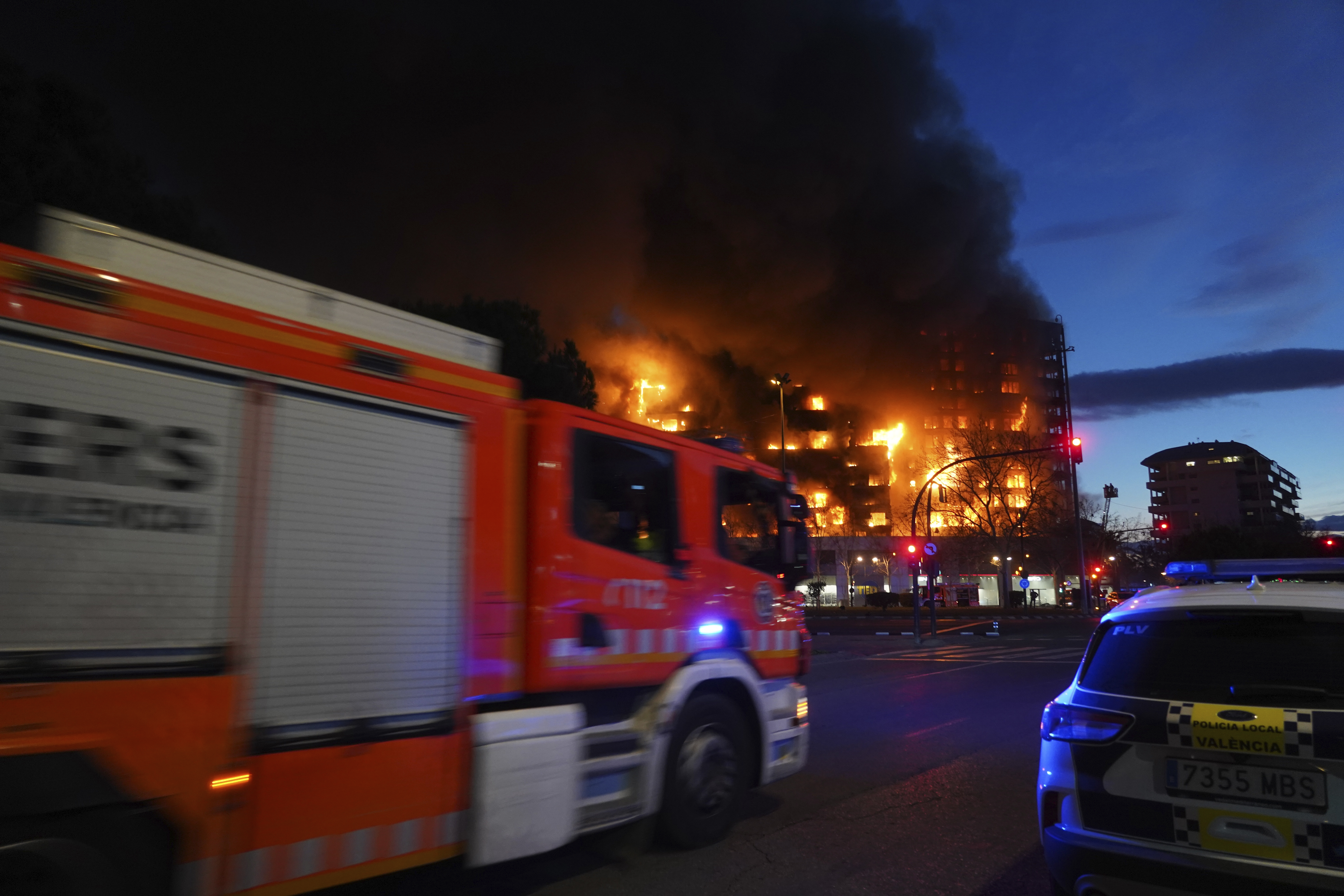 A fire engine and a police car are parked outside a housing block on fire in Valencia, Spain, Thursday, Feb. 22, 2024. The cause of the fire is unknown and if there are any victims. (AP Photo/Alberto Saiz)