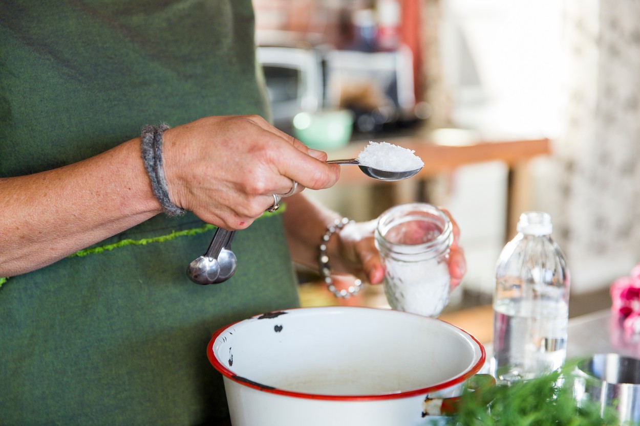 Hand of woman adding sea salt to bowl in kitchen