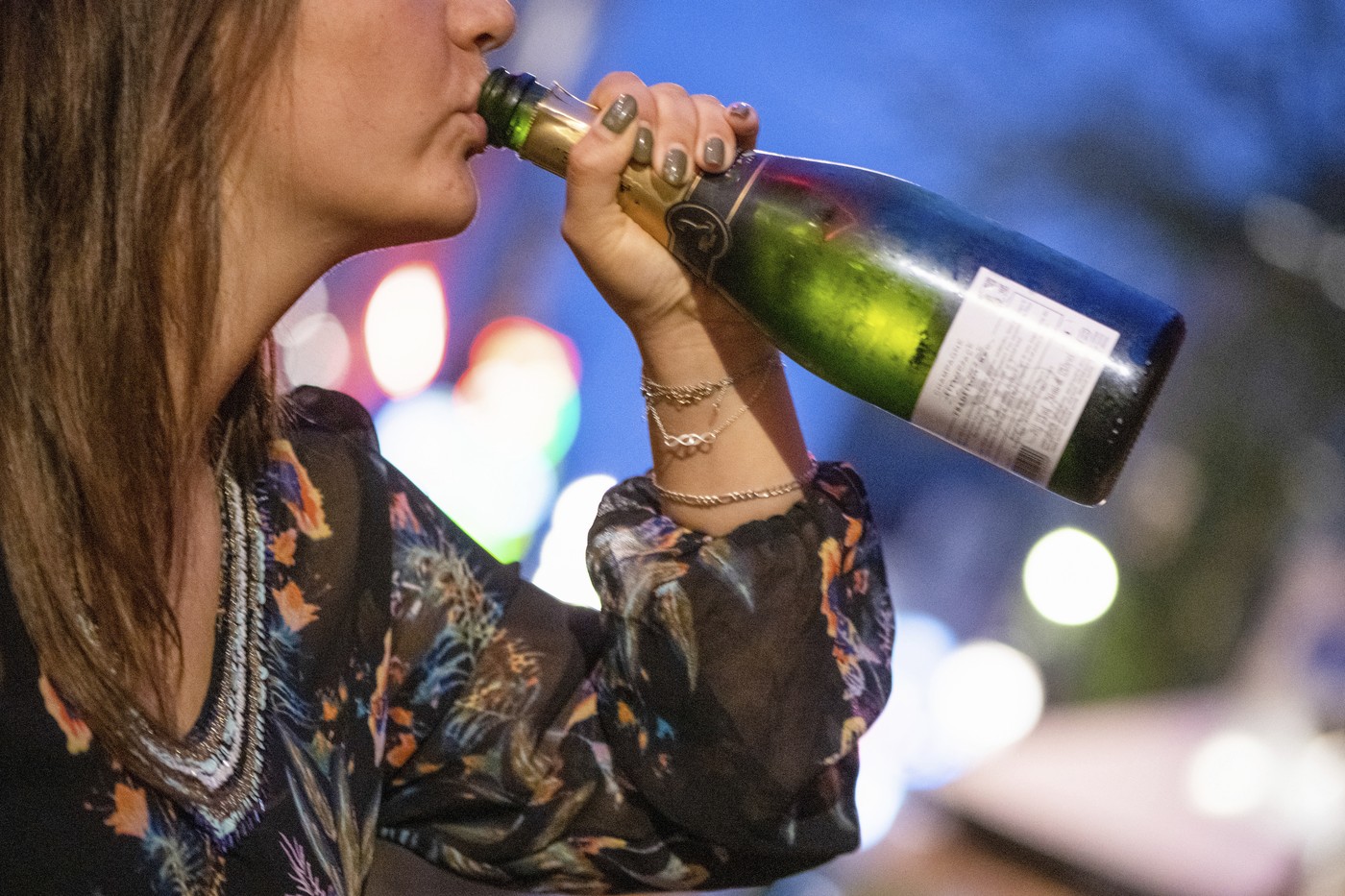 Woman casually drinking from a wine bottle outdoors at night.