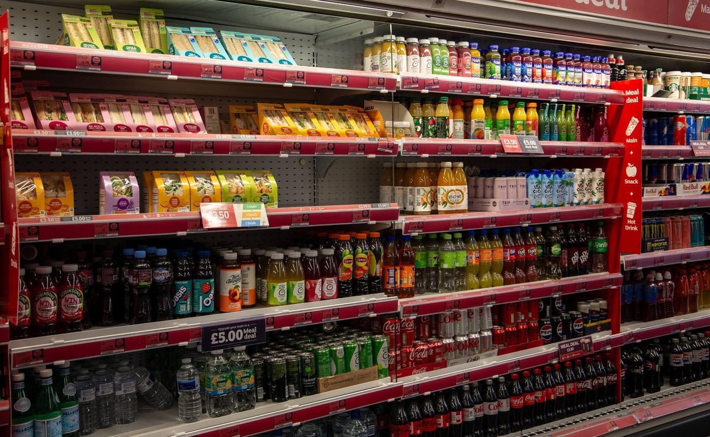 Full shelves of various beverages and juices in a supermarket with price tags and meal deal sign
