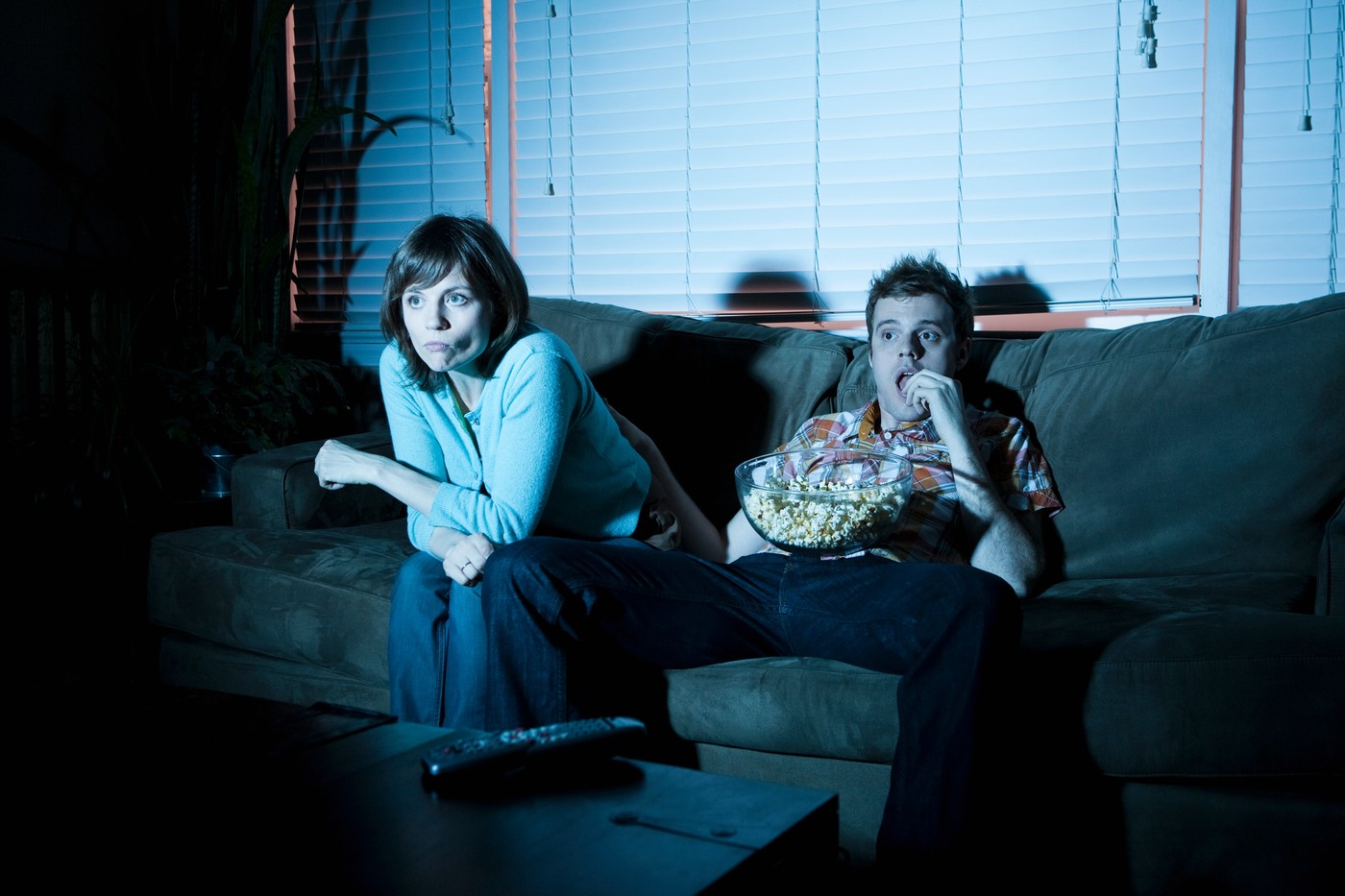 Young couple watching tv, man eating popcorn