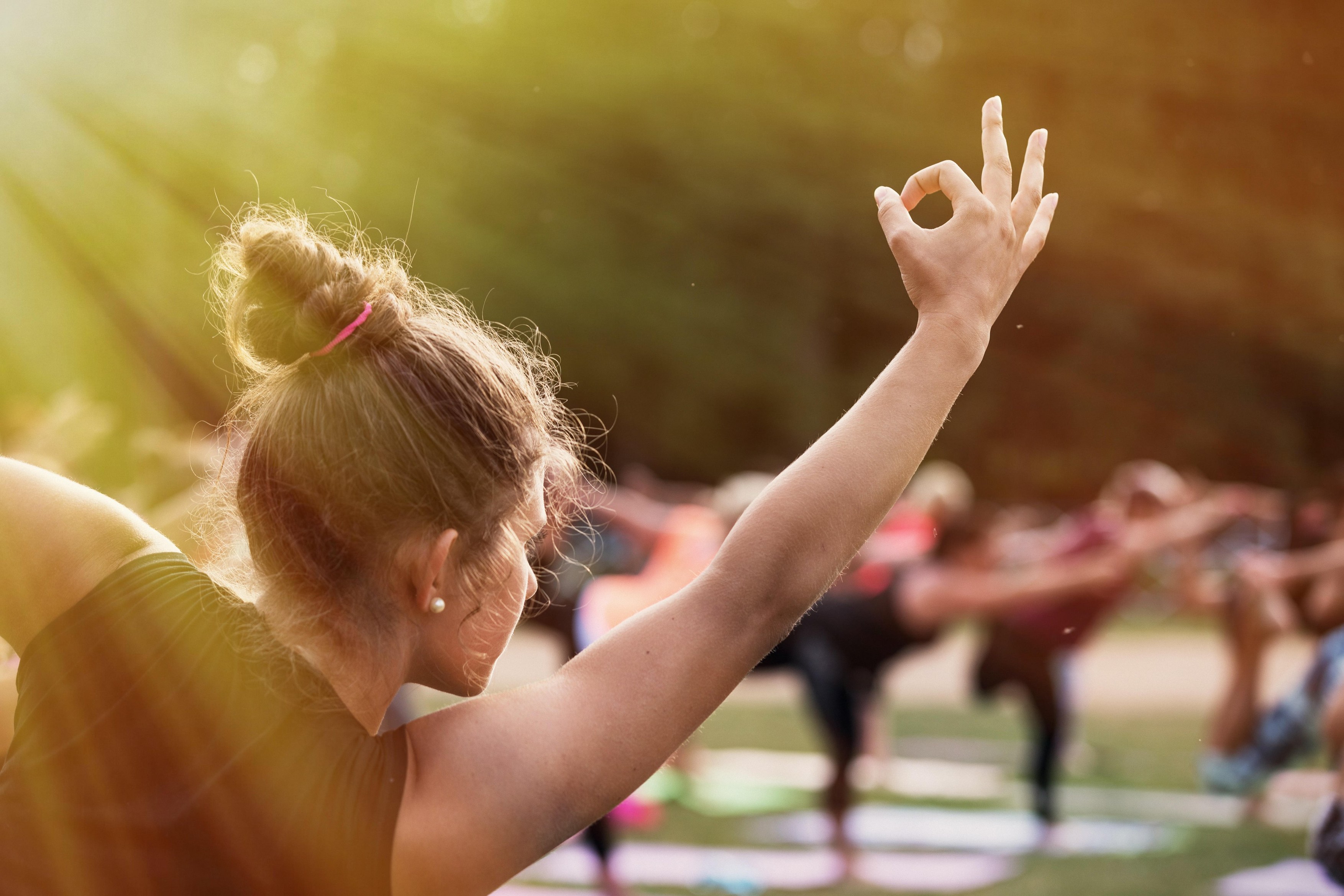 Woman practicing yoga on a meadow. In backround group of women practicing yoga together during a beautiful sunny day on the meadow. Yoga in nature. Co