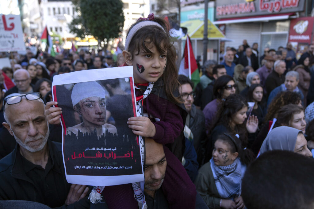 A girl carries a poster with Arabic writing that reads "a general strike in all over the world," during a rally in solidarity with Gaza, in the West Bank city of Ramallah, Monday, Dec. 11, 2023. (AP Photo/Nasser Nasser)