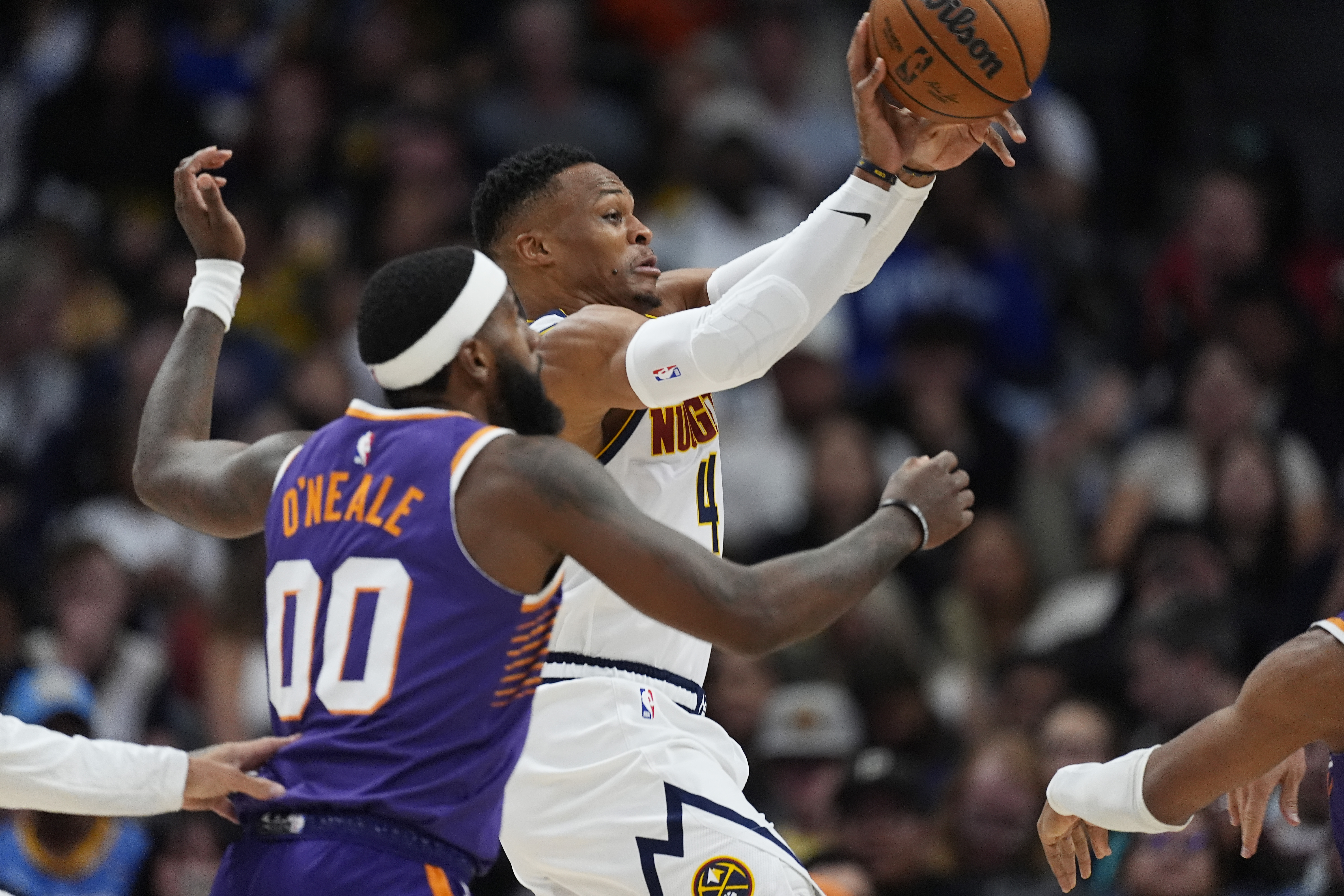 Denver Nuggets guard Russell Westbrook, back, passes the ball as Phoenix Suns forward Royce O'Neale defends in the second half of an NBA preseason game, Sunday, Oct. 13, 2024, in Denver. (AP Photo/David Zalubowski)