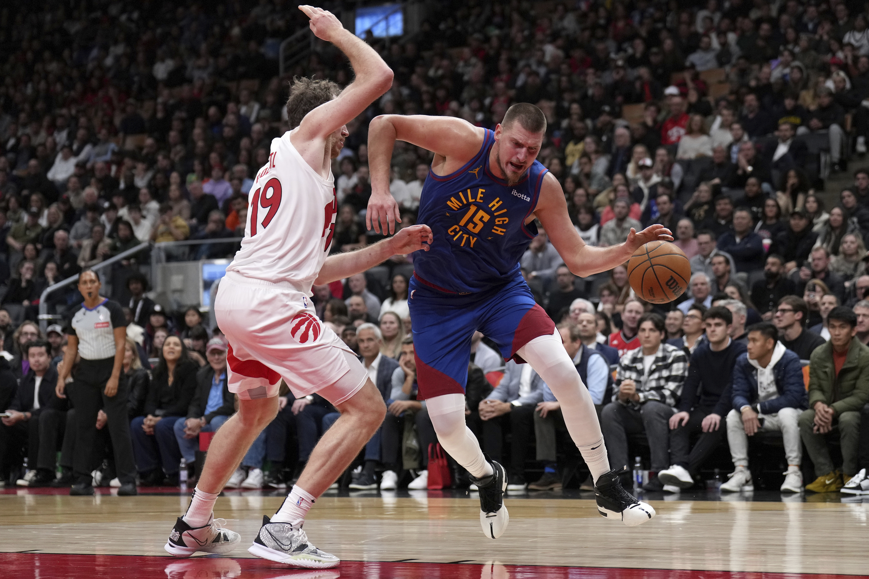 Denver Nuggets center Nikola Jokic (15) dribbles past Toronto Raptors center Jakob Poeltl (19) during second-half NBA basketball game action in Toronto, Monday, Oct. 28, 2024. (Nathan Denette/The Canadian Press via AP)