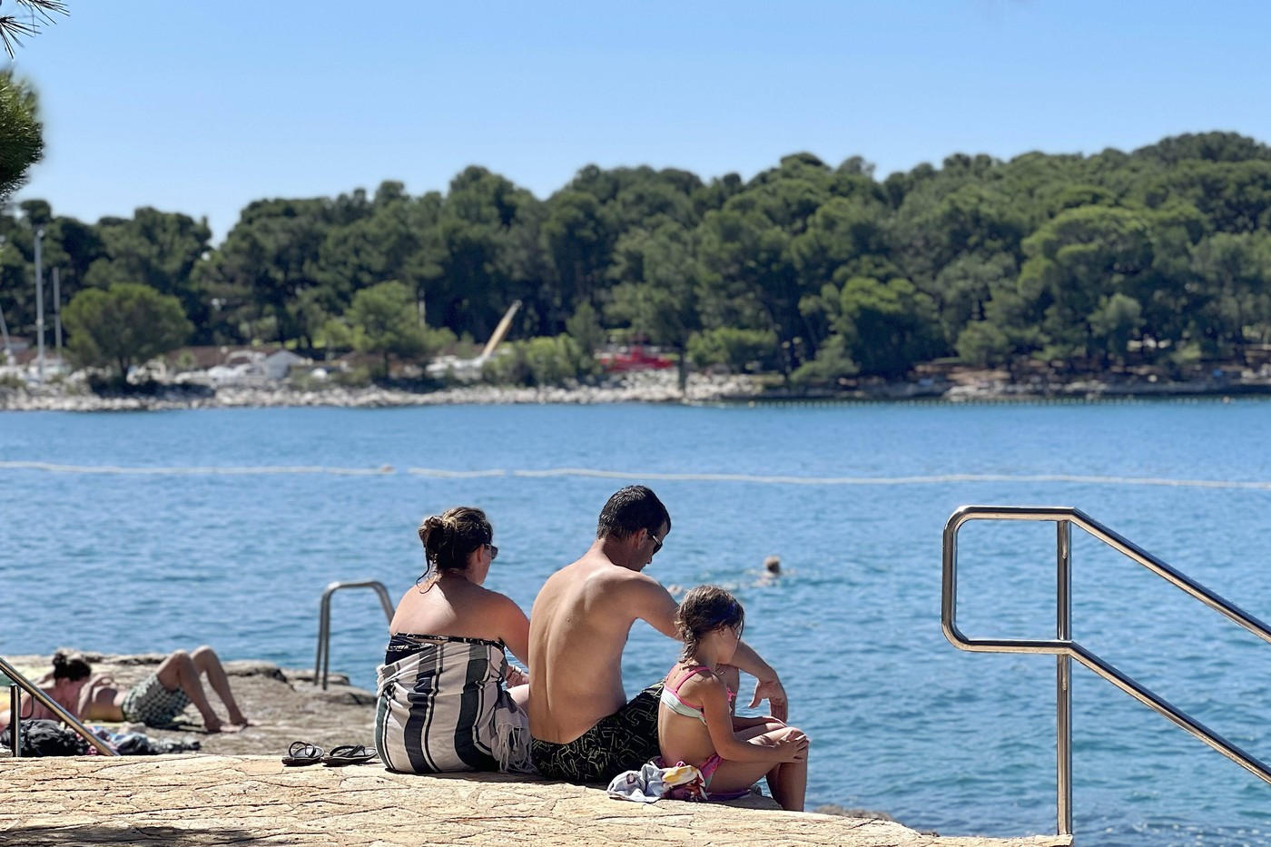 Plava Laguna,Adriakueste bei Porec / Kroatien,Strand. Urlauber,Familie,Eltern mit einem Kind sitzen am Steinstrand,Felss
