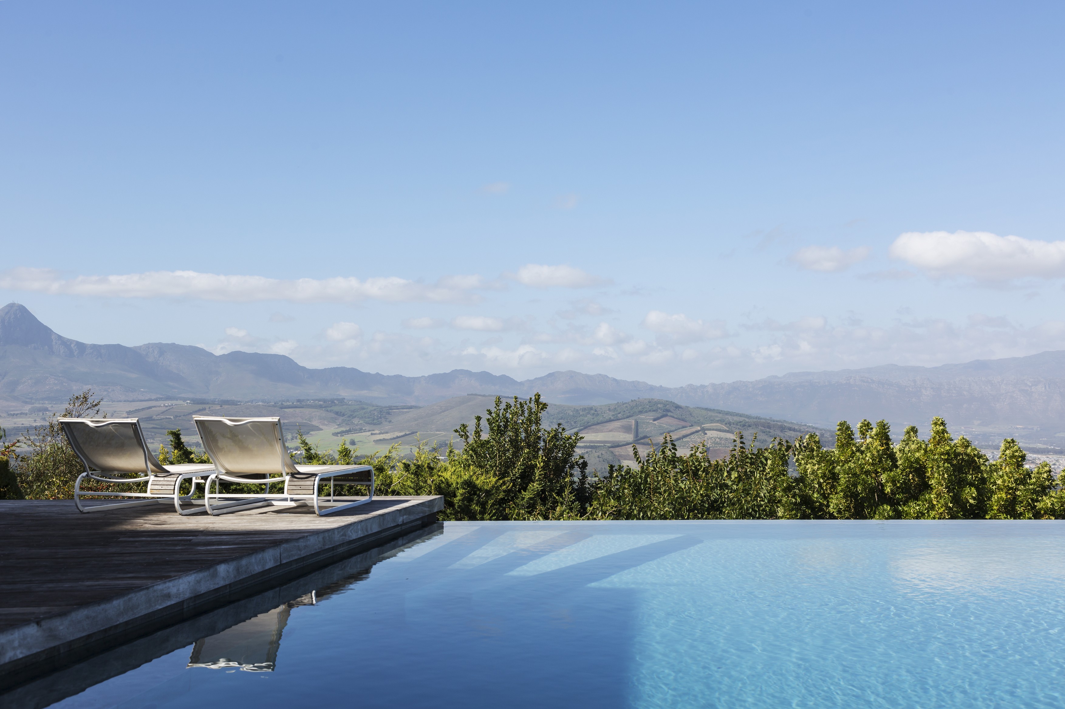 Luxury infinity pool and lounge chairs with mountain view under sunny, blue sky