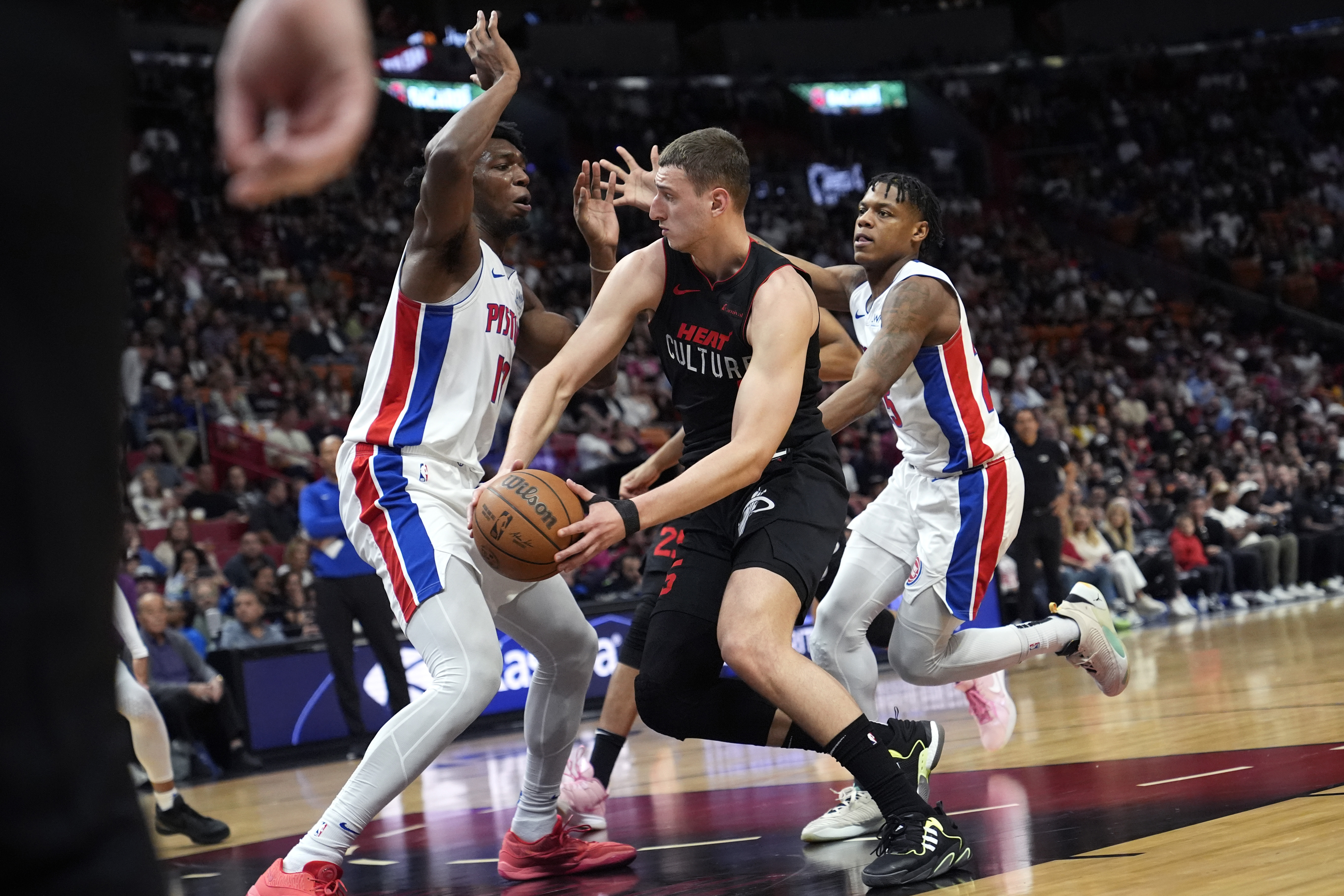 Miami Heat forward Nikola Jovic, center, looks to pass the ball as Detroit Pistons center James Wiseman, left, defends during the first half of an NBA basketball game Tuesday, March 5, 2024, in Miami. (AP Photo/Lynne Sladky)