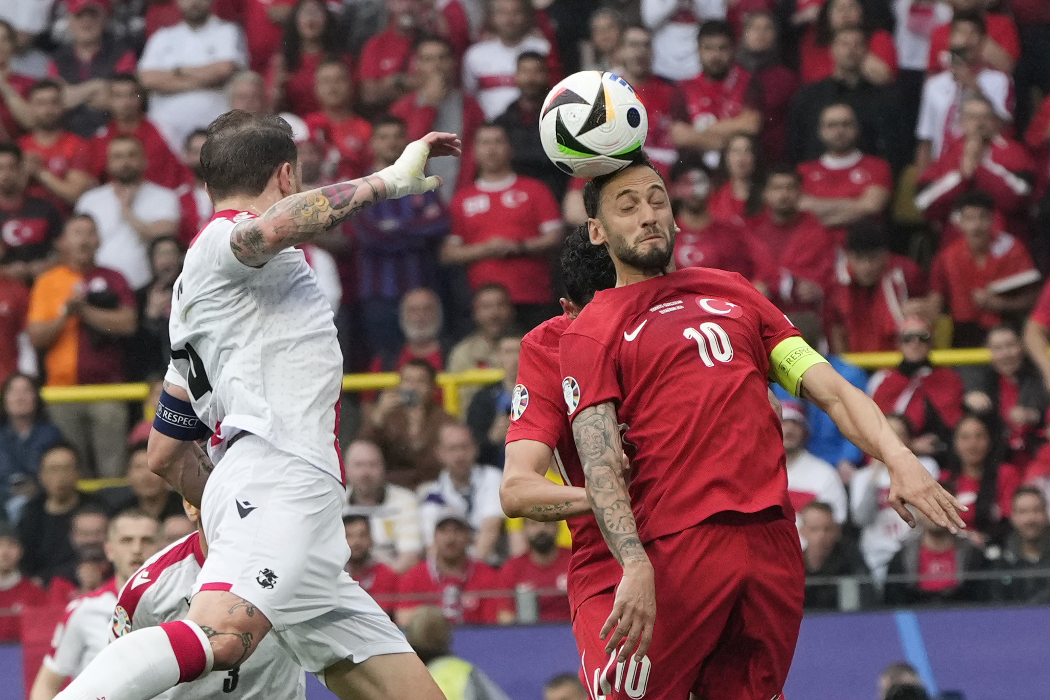 Turkey's Hakan Calhanoglu, right, jumps for the ball with Georgia's Giorgi Kochorashvili during a Group F match between Turkey and Georgia at the Euro 2024 soccer tournament in Dortmund, Germany, Tuesday, June 18, 2024. (AP Photo/Alessandra Tarantino)