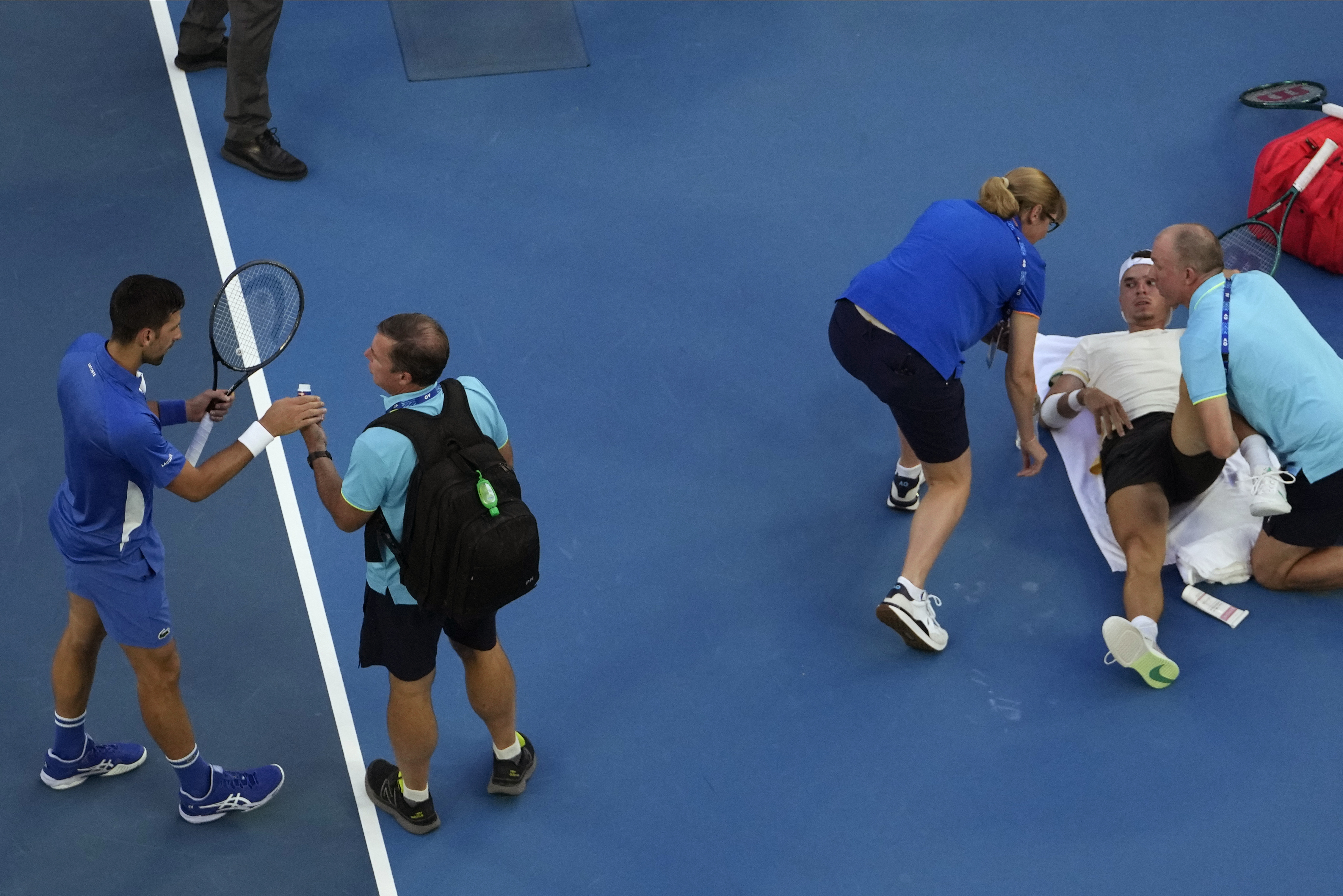 Croatia's Dino Prizmic receives treatment from a trainer during his first round match against Serbia's Novak Djokovic, left, at the Australian Open tennis championships at Melbourne Park, Melbourne, Australia, Sunday, Jan. 14, 2024. (AP Photo/Andy Wong)