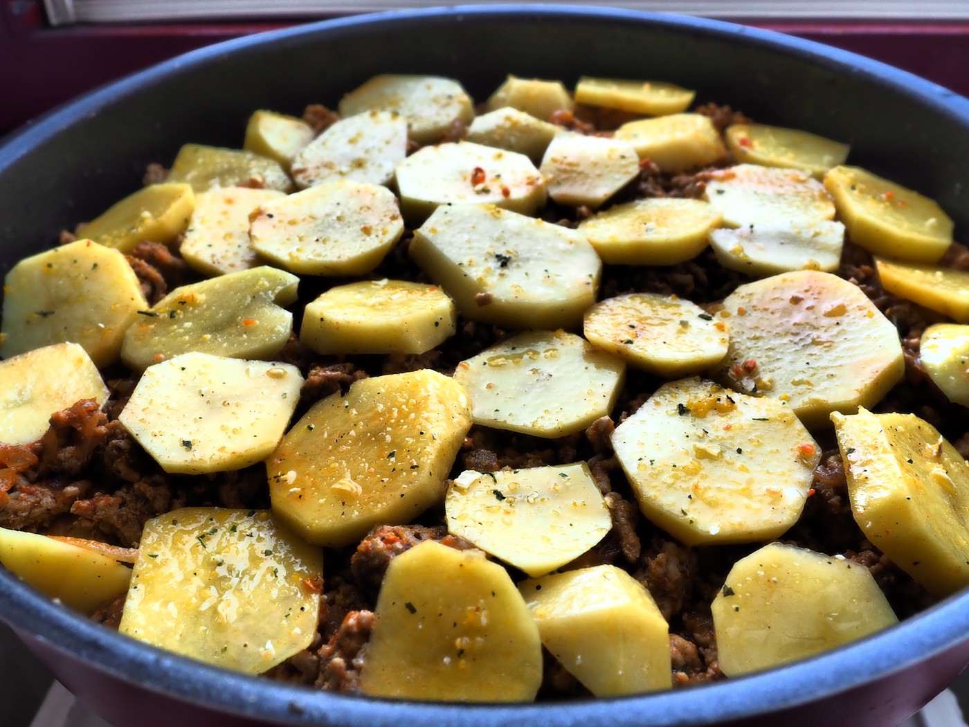 Raw potatoes, cut into circles and stacked on top of minced meat and onions. Moussaka making process. Spices on potatoes. Balkan cuisine - traditional Greek, Serbian and Turkish food