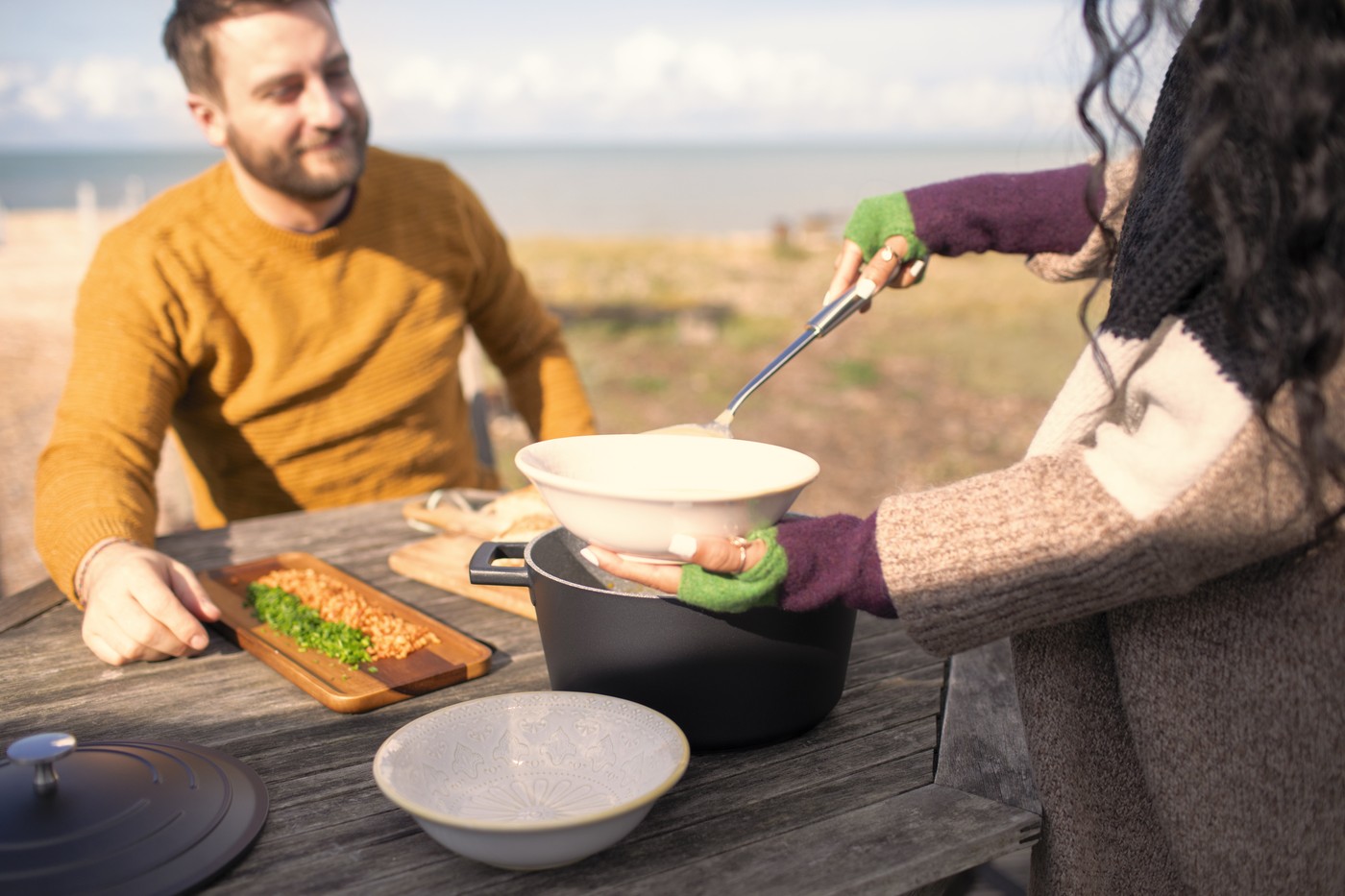 Woman serving chowder to. boyfriend on sunny beach patio