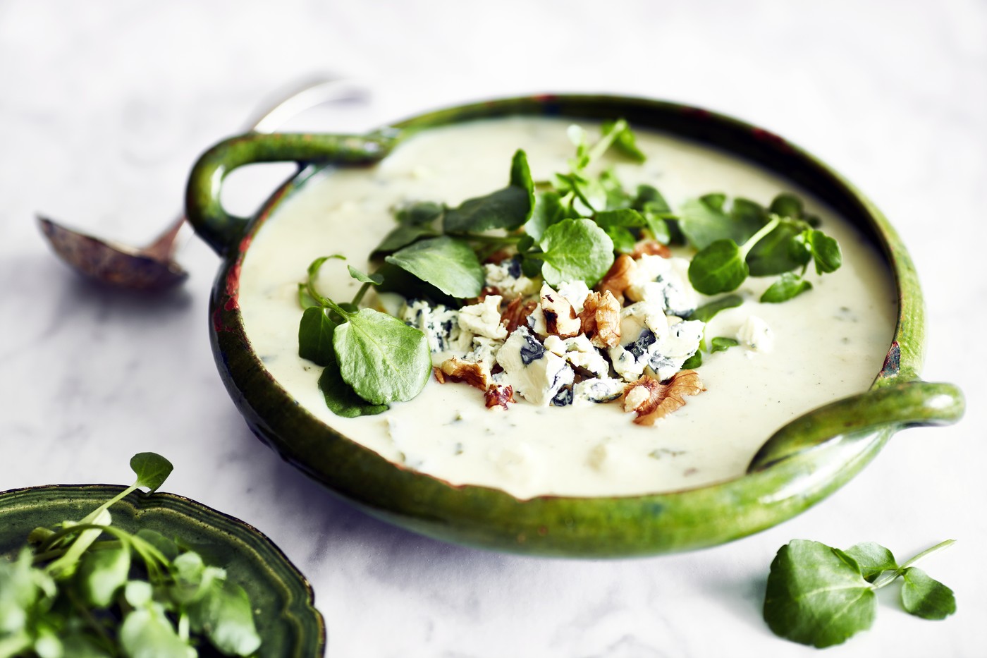 Bowl of soup garnished with blue cheese, walnut and watercress