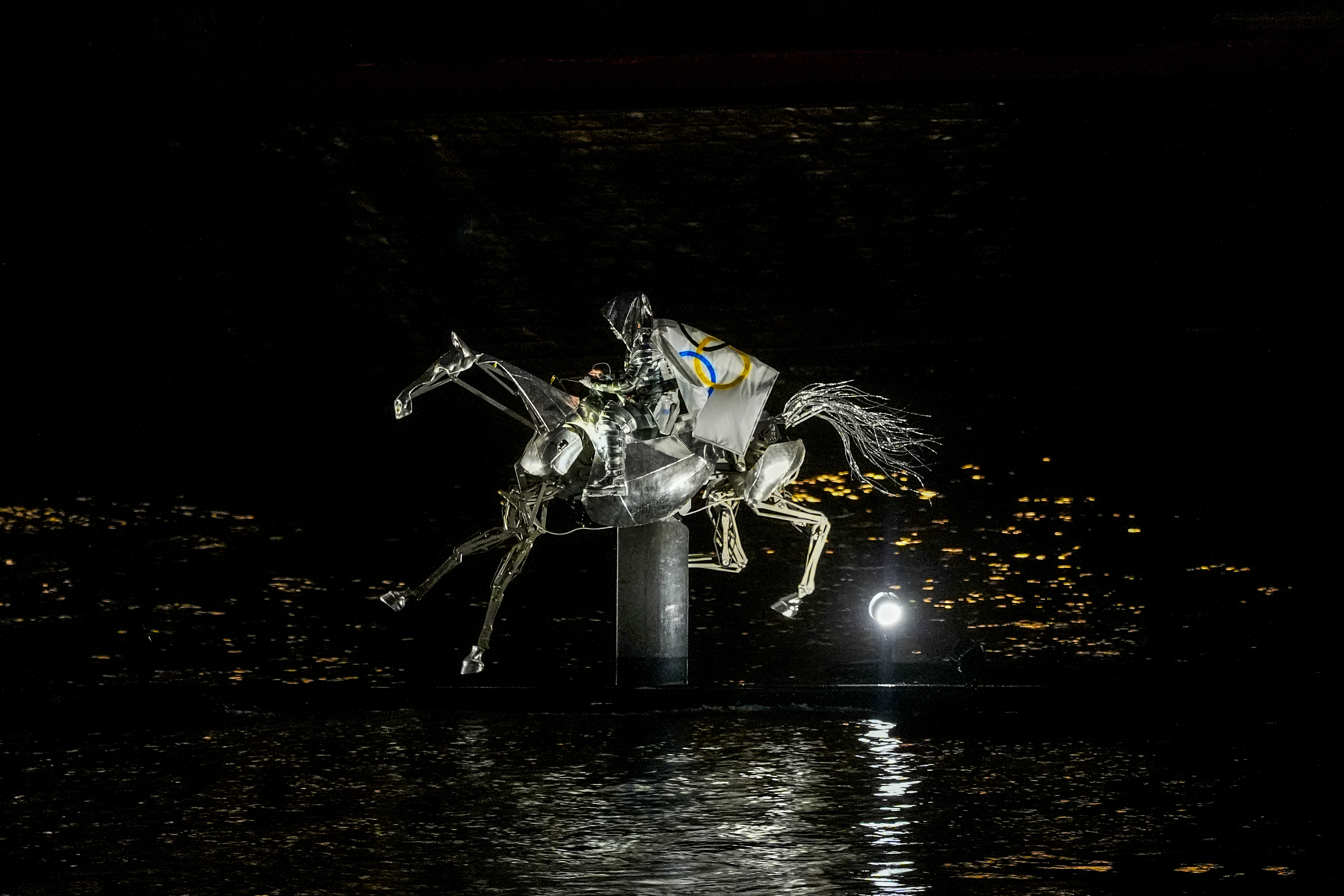 A performer on a mechanical horse carries the Olympic flag down the river Seine in Paris, France, during the opening ceremony of the 2024 Summer Olympics, Friday, July 26, 2024. (AP Photo/Lindsey Wasson)