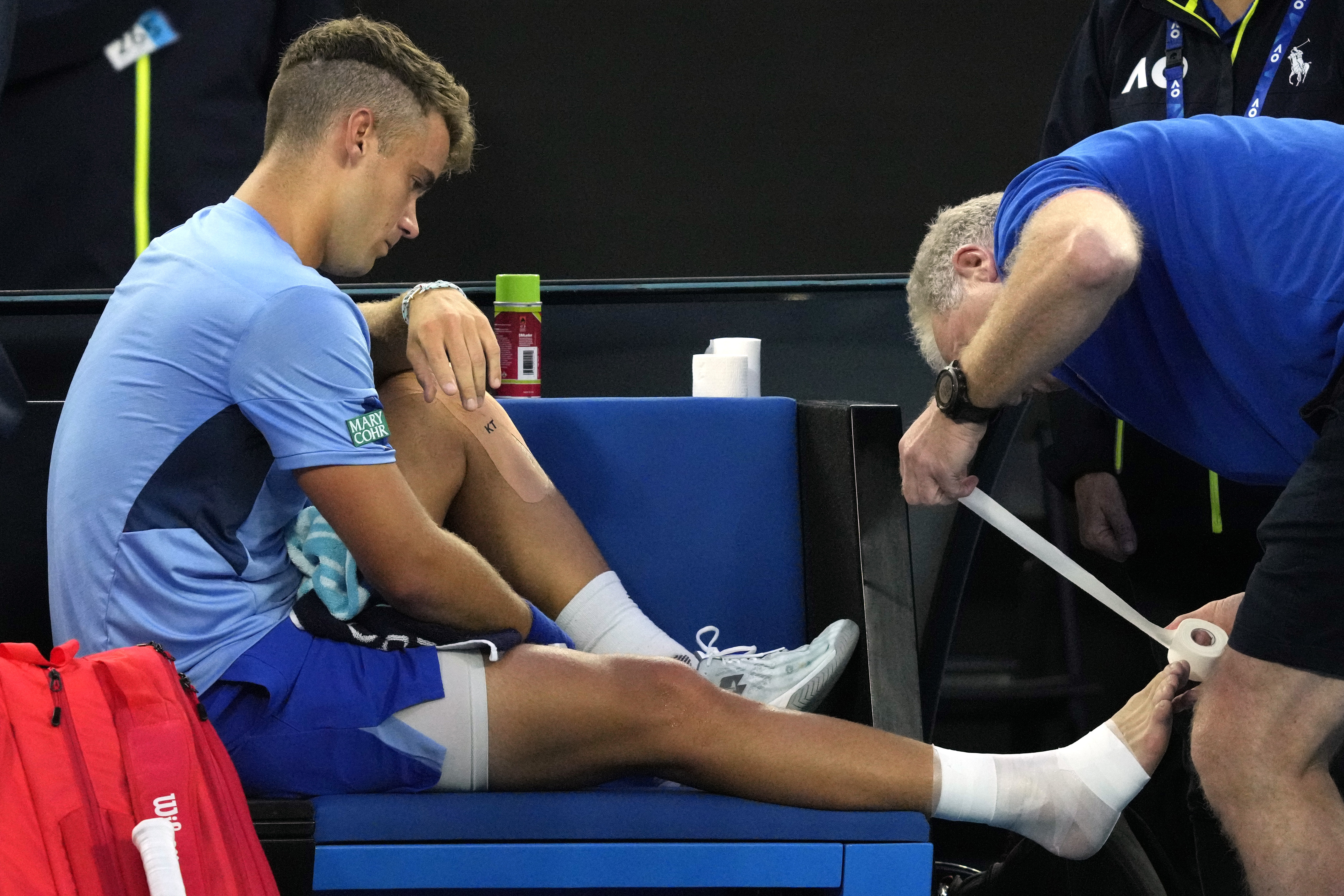 Enzo Couacaud of France has his ankle taped during his second round match against Novak Djokovic of Serbia at the Australian Open tennis championship in Melbourne, Australia, Thursday, Jan. 19, 2023. (AP Photo/Dita Alangkara)