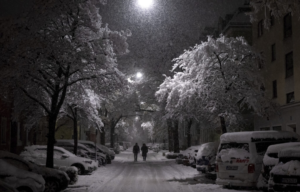 Pedestrians stroll down a snow-covered street, Friday evening, Dec. 1, 2023, in Munich. (Sven Hoppe/dpa/dpa via AP)